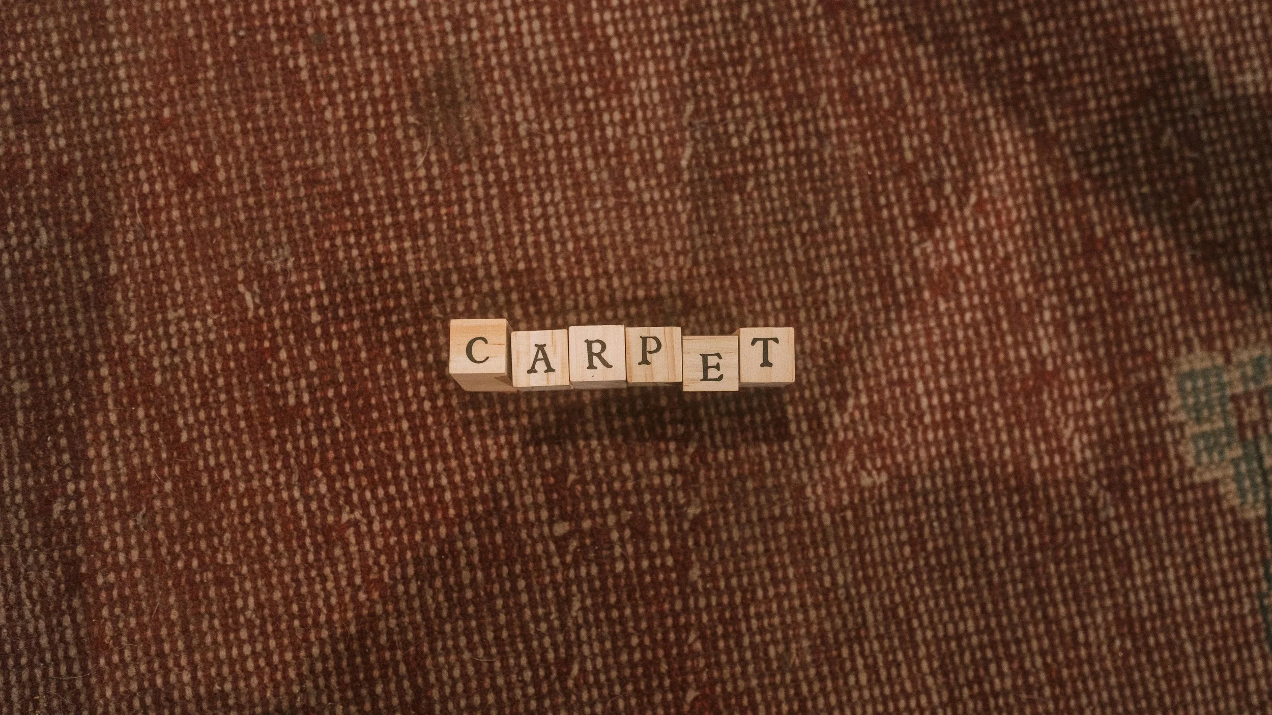 Scrabble tiles spelling 'CARPET' on a textured brown fabric surface.