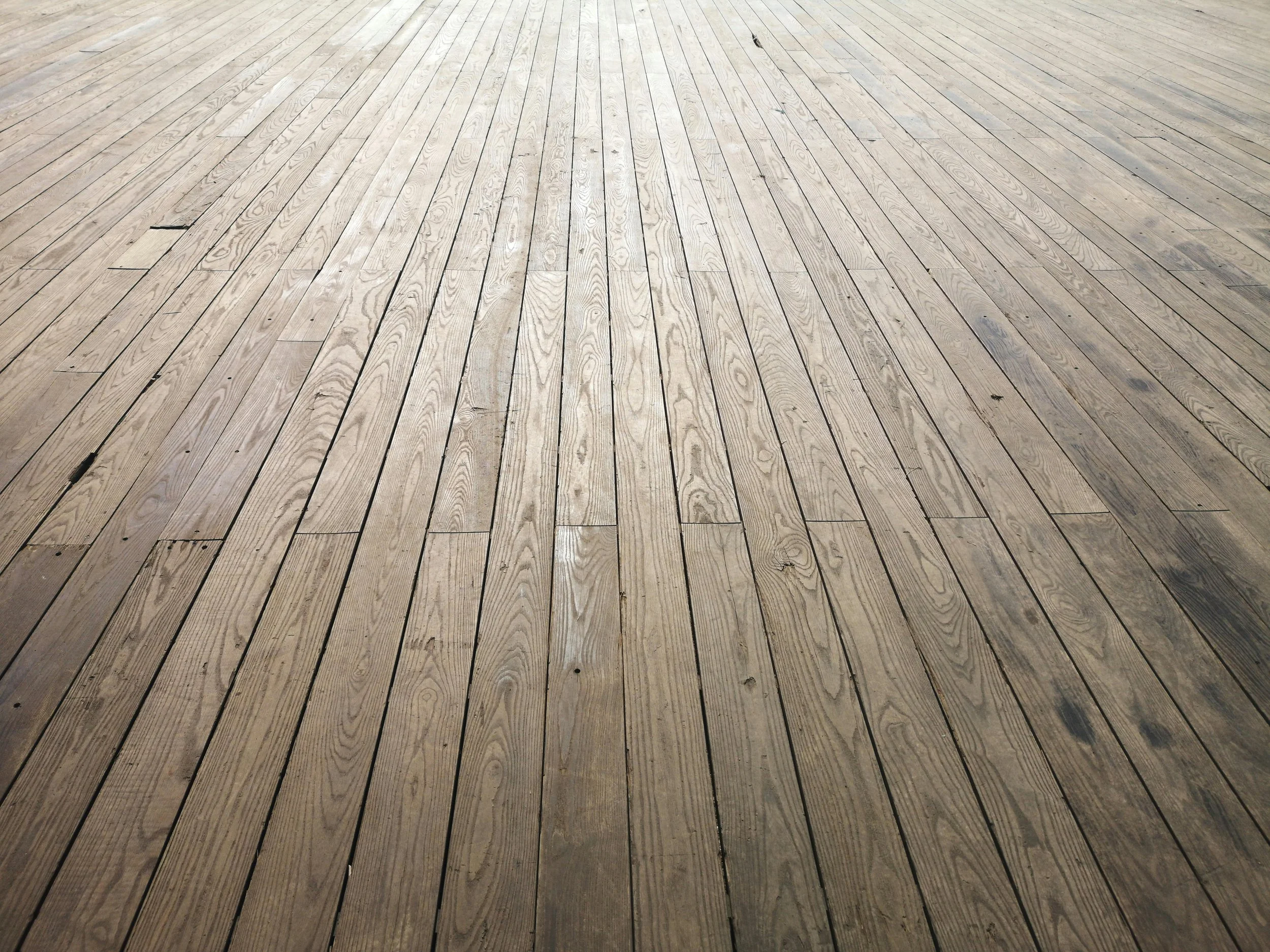 A wooden deck with parallel planks, some with visible wood grain and slight discoloration.