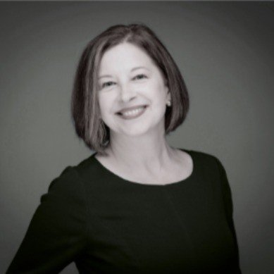 Black and white portrait of a woman smiling, with shoulder-length hair, wearing a dark top against a plain background.