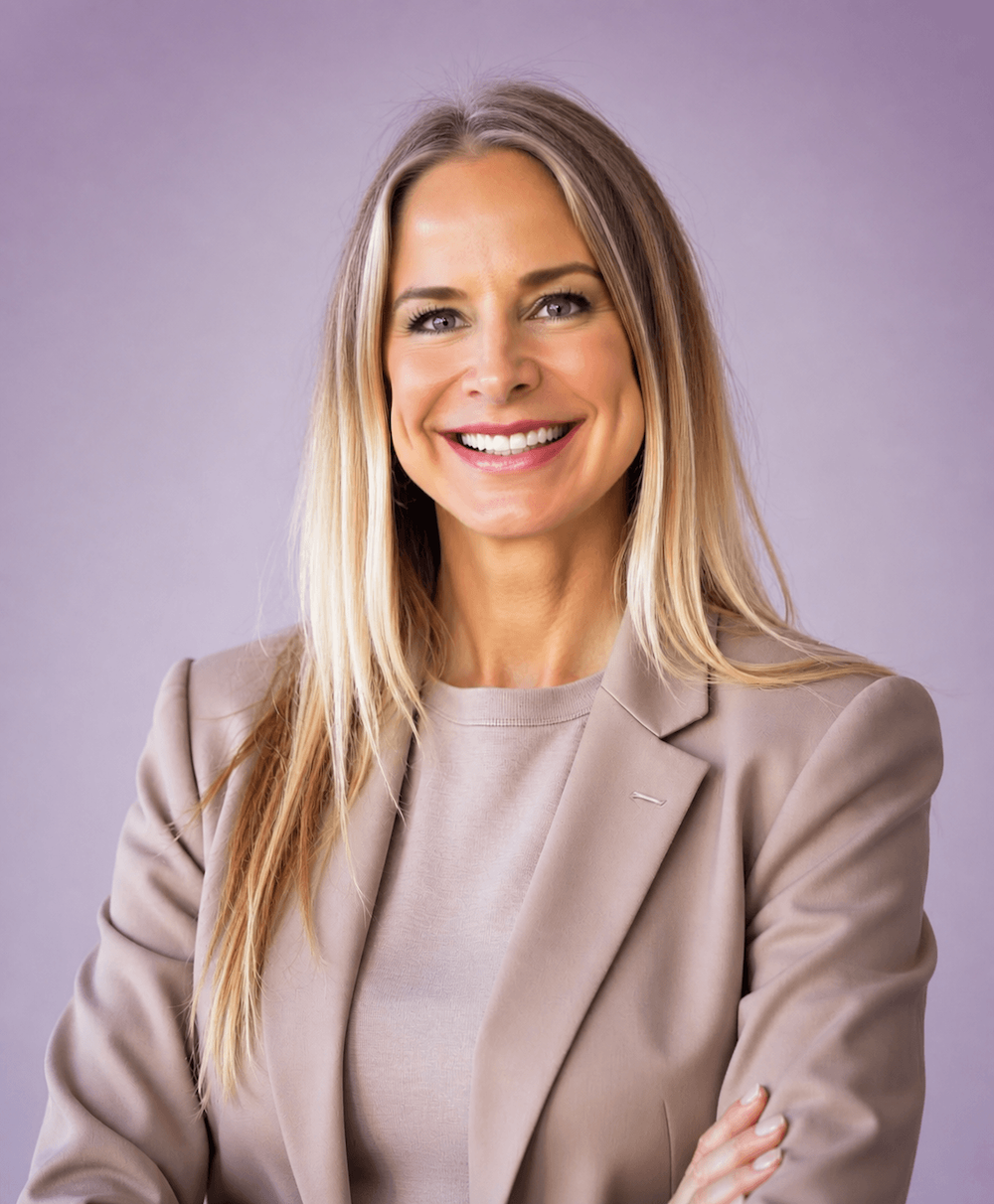 Jeanine Pearce Clarke wearing a beige blazer and beige shirt, with her arms crossed, against a light gray background.