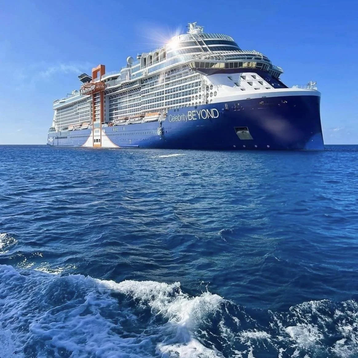 Large cruise ship named Celebrity Beyond sailing on the ocean under a clear blue sky.
