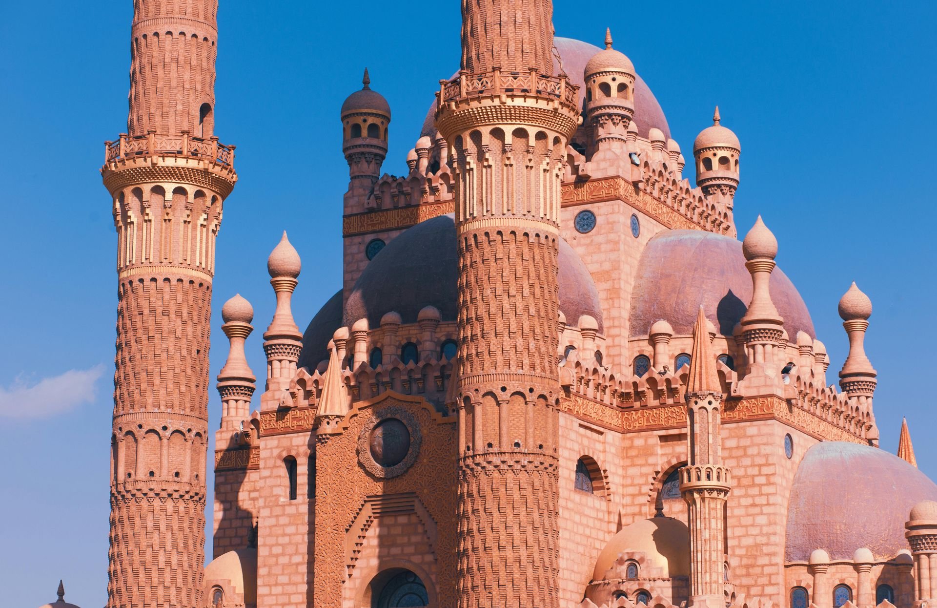 Pink castle with multiple turrets and minarets against a blue sky.