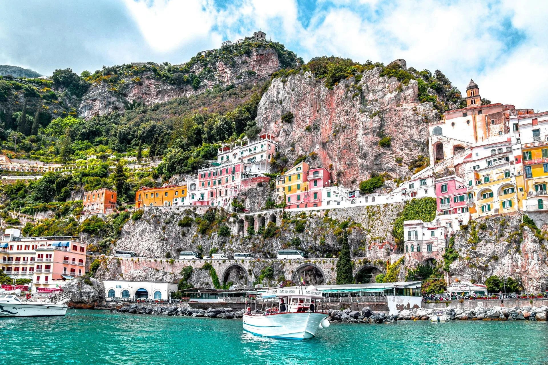 Colorful buildings along a rocky hillside overlooking the waterfront with boats in the turquoise water.