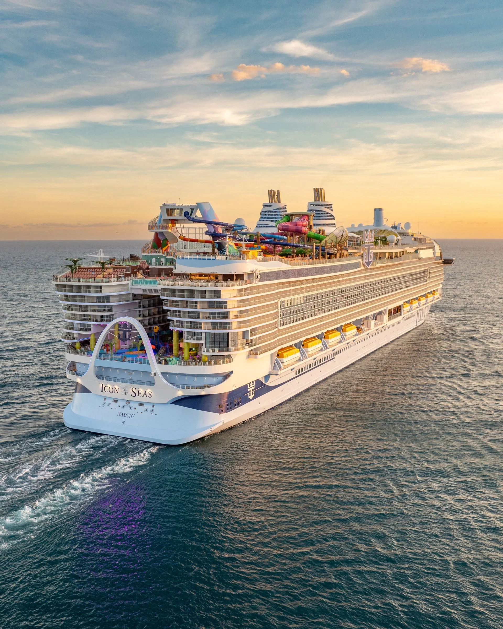 Large cruise ship named 'Icon of the Seas' sailing on the ocean during sunset, with water slides and pool areas on top deck.