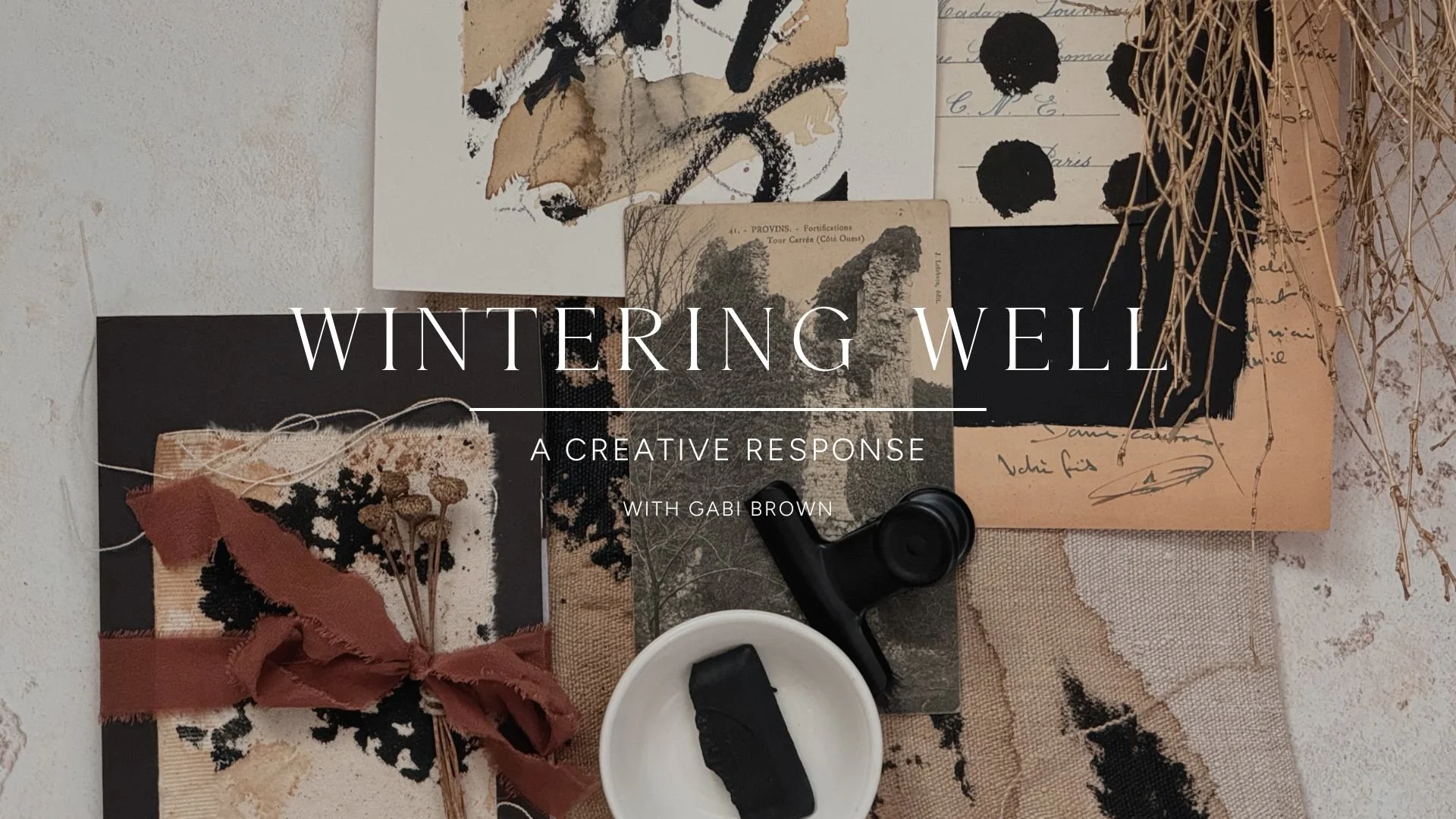 Flat lay of artwork, papers, dried flowers tied with ribbon, a black tape dispenser, and a white cup with black substance on a textured surface, with overlaid text reading 'Wintering Well: A Creative Response with Gabi Brown'.