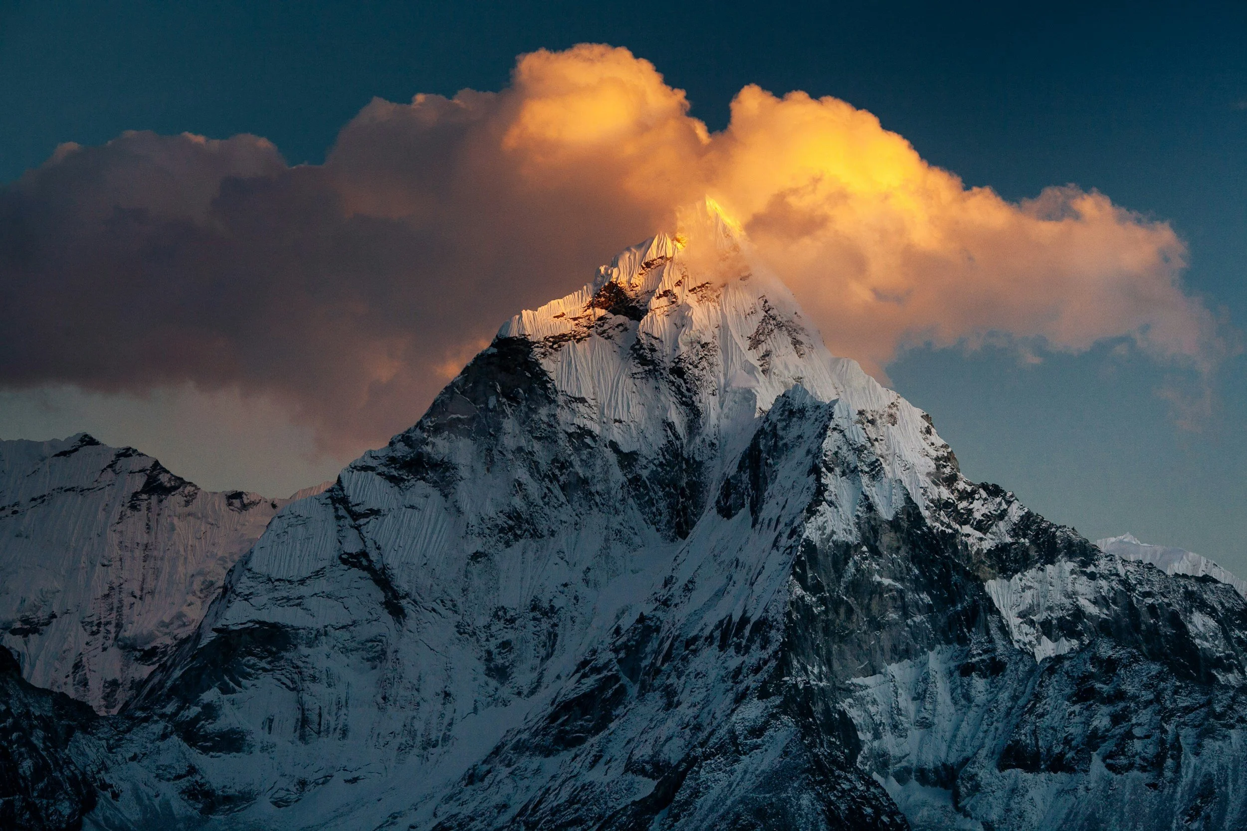 Snow-capped mountain peak of the Himalayas in the Annapurna area at sunset with clouds illuminated in orange and pink hues in the sky.