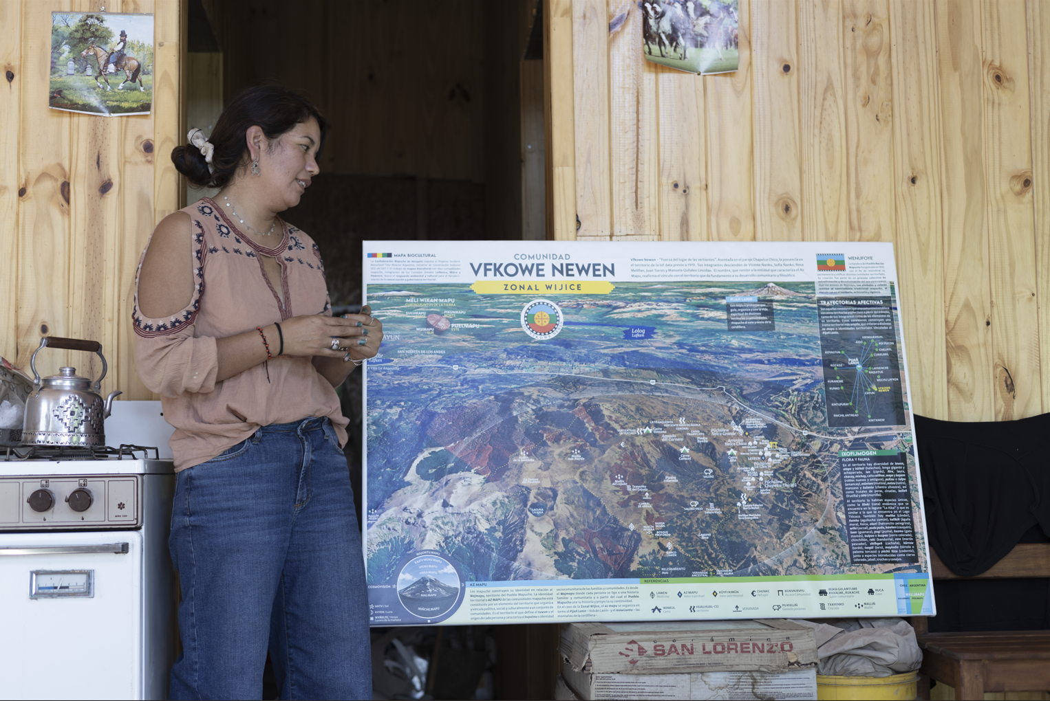 Group of four people sitting outdoors on grass, engaged in conversation, with a house, trees, and mountains in the background.