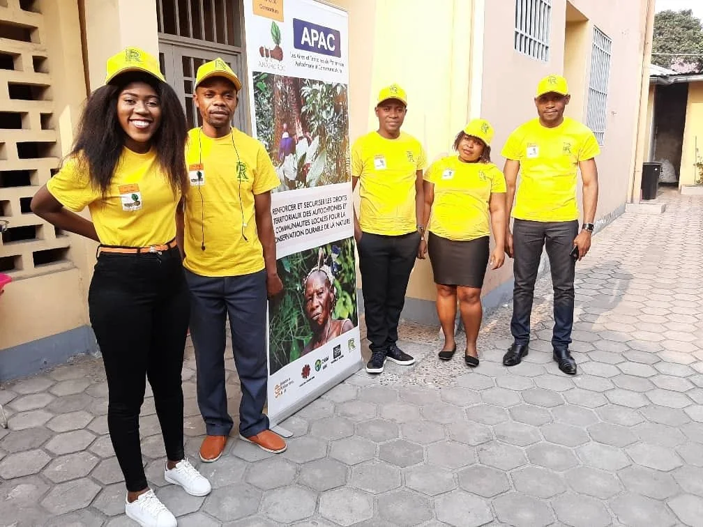 Five people wearing yellow shirts and hats standing beside a banner about sustainable agriculture in the DRC.