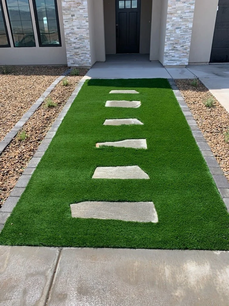 Artificial grass walkway with stepping stones leading to the front door of a modern house.