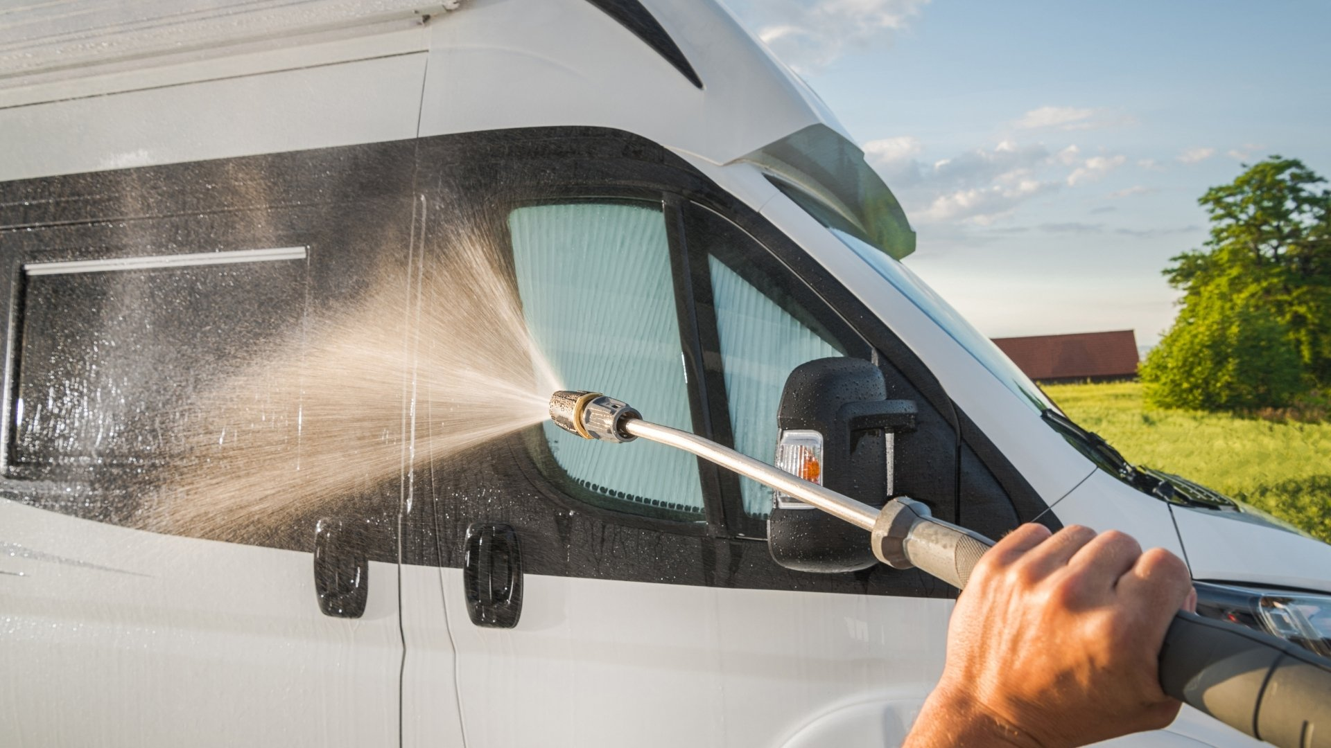 Person pressure washing the side of a white van with a spray wand on a sunny day.