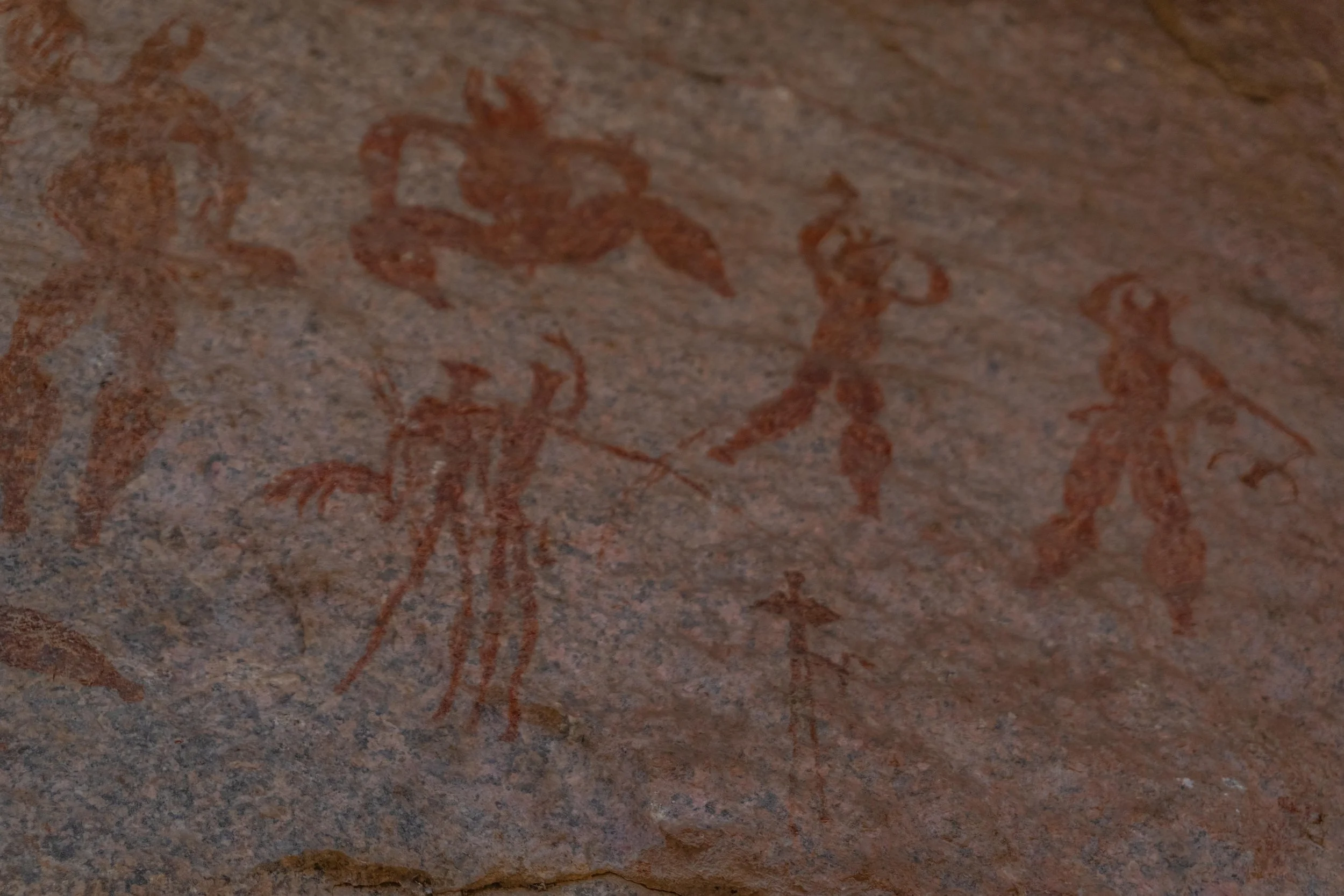 Ancient cave paintings depicting human figures on a reddish-brown rock surface.
