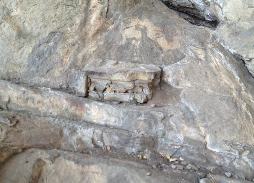 A small stone structure built into a rock face, resembling a miniature bench or altar, with rocks and debris around it.