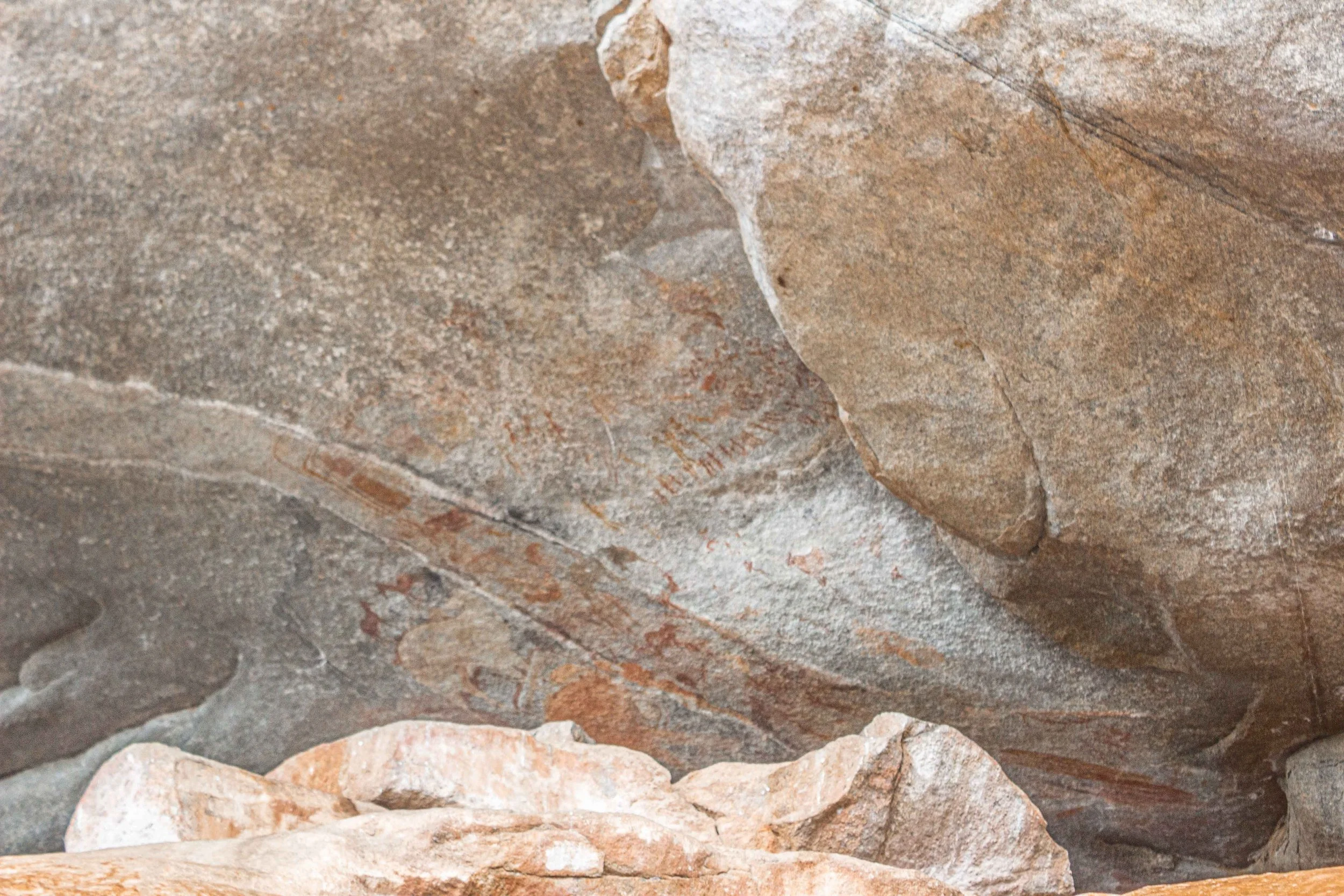 Close-up of ancient rock carvings on a stone wall, including faint red markings and engravings.