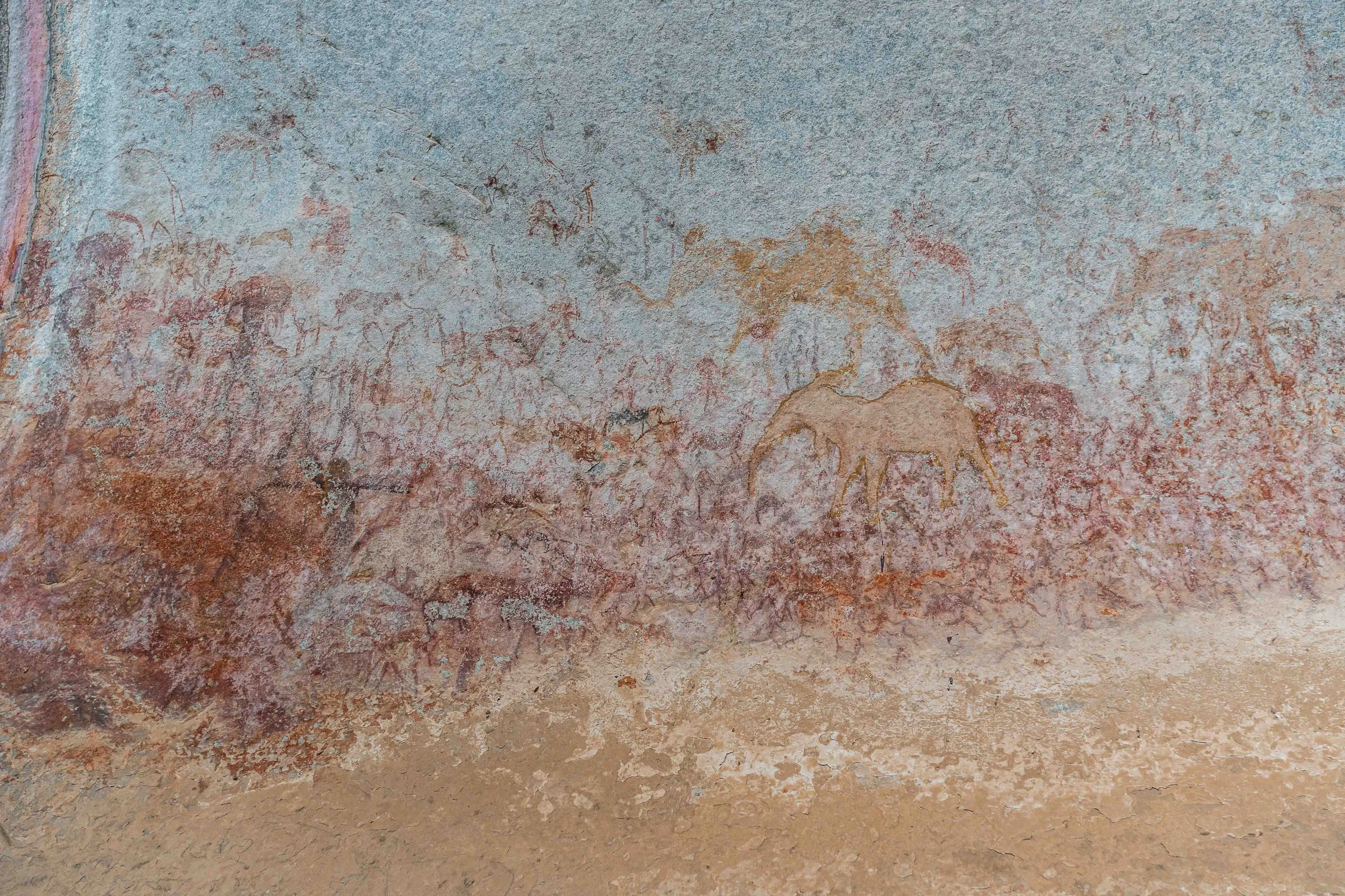 Ancient cave painting depicting a herd of animals, including a prominently drawn elephants and other figures, on a rough, speckled rock surface.