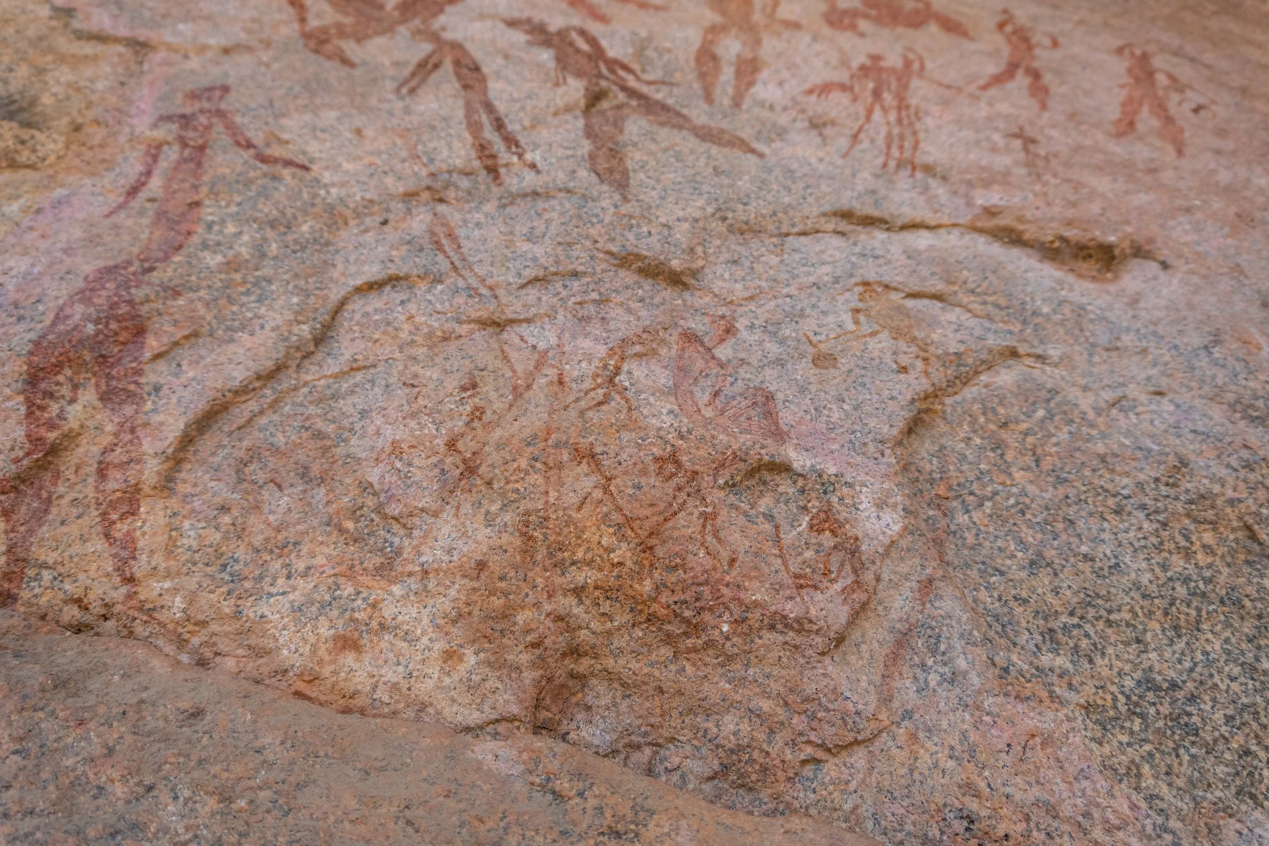 Ancient cave painting of human figures on reddish rock surface.