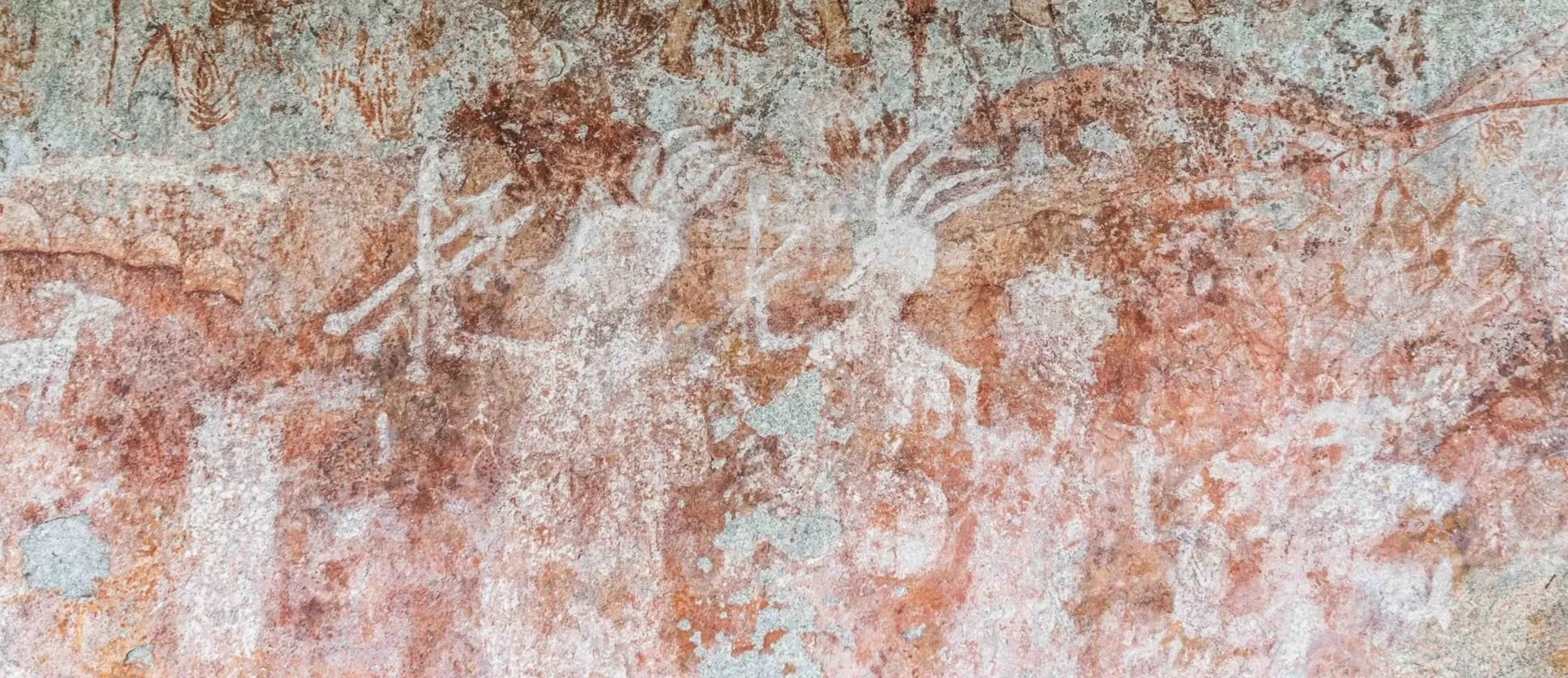 Ancient cave painting depicting animals and humans in reddish-brown and white pigments.