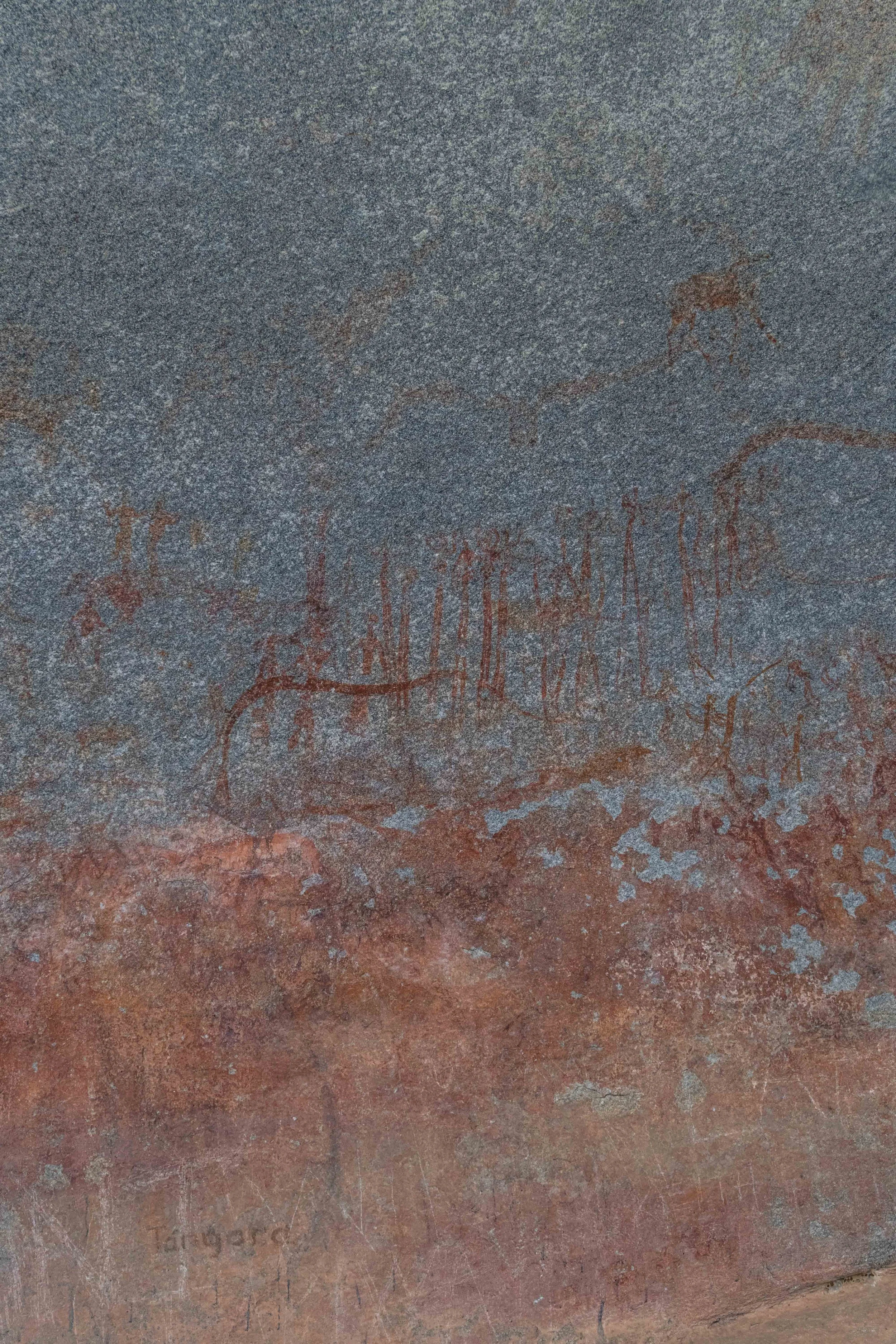 Ancient rock surface with petroglyph carvings of animals, including a deer, on the lower part, with layered reddish and grayish stone textures.