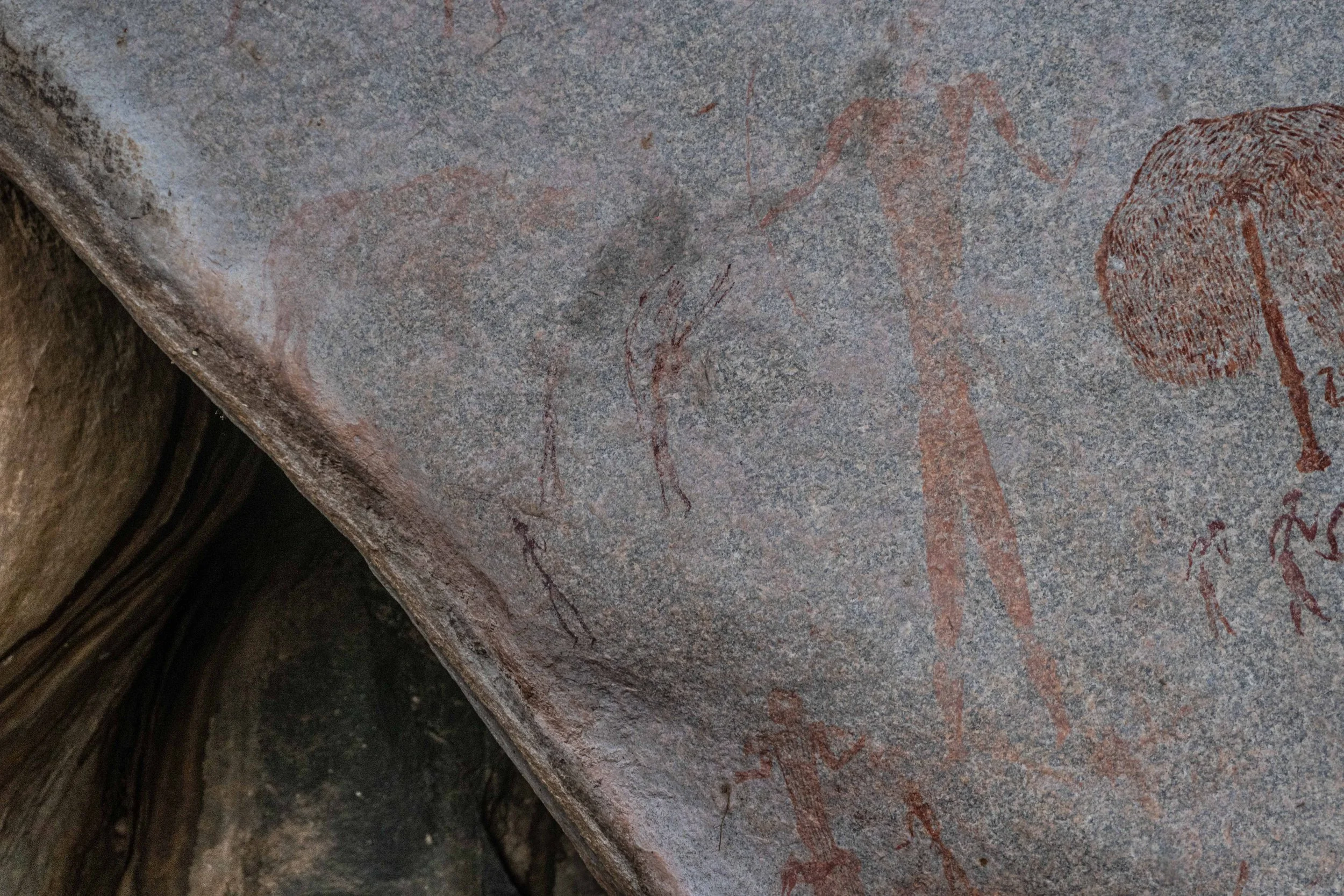 Ancient cave paintings of human figures, animals, and symbols on a rock surface.