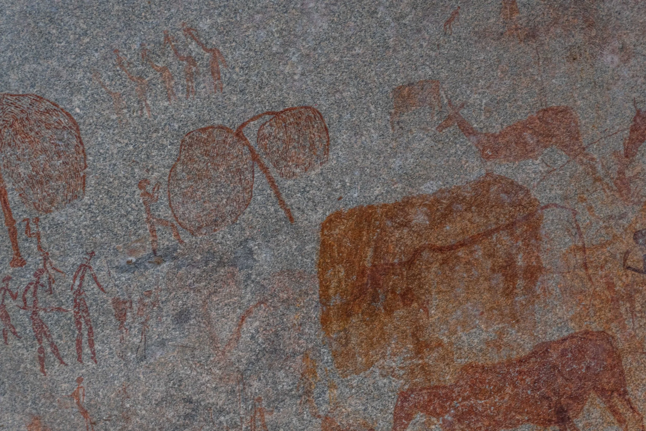Ancient cave paintings on a rock wall, depicting human figures and animals in red pigment.