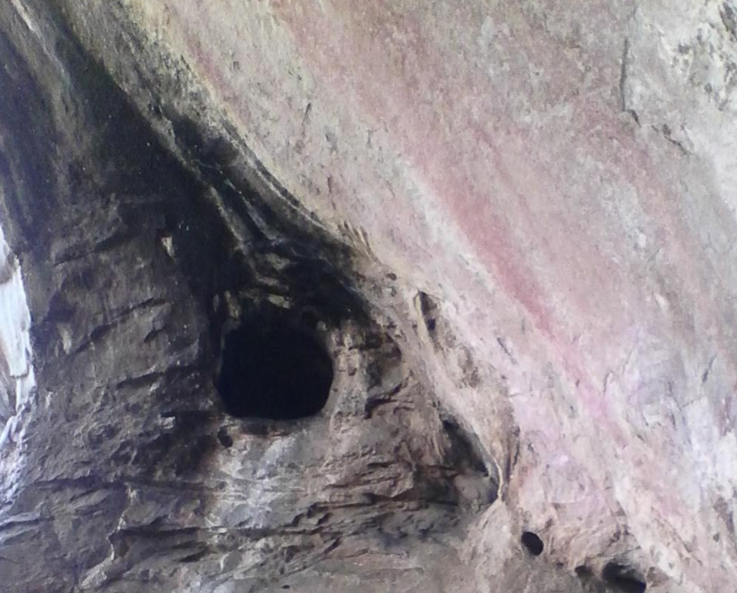 Close-up of a weathered rock face with a geological tunnel covered by soot