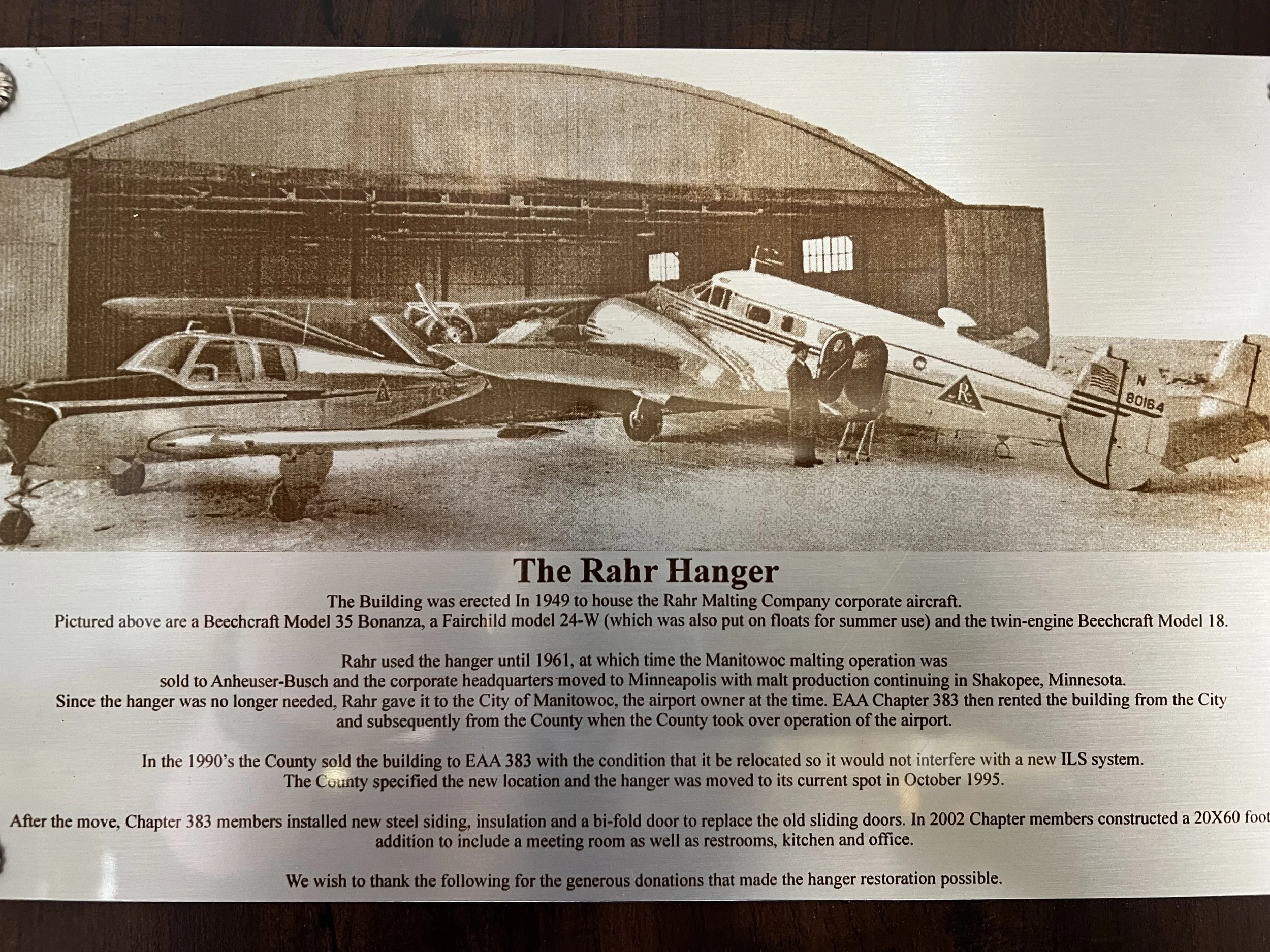 A sepia-toned historical photograph of three vintage aircraft inside a hangar. The aircraft include a Beechcraft Model 35 Bonanza, a Fairchild Model 24-W, and a twin-engine Beechcraft Model 18.