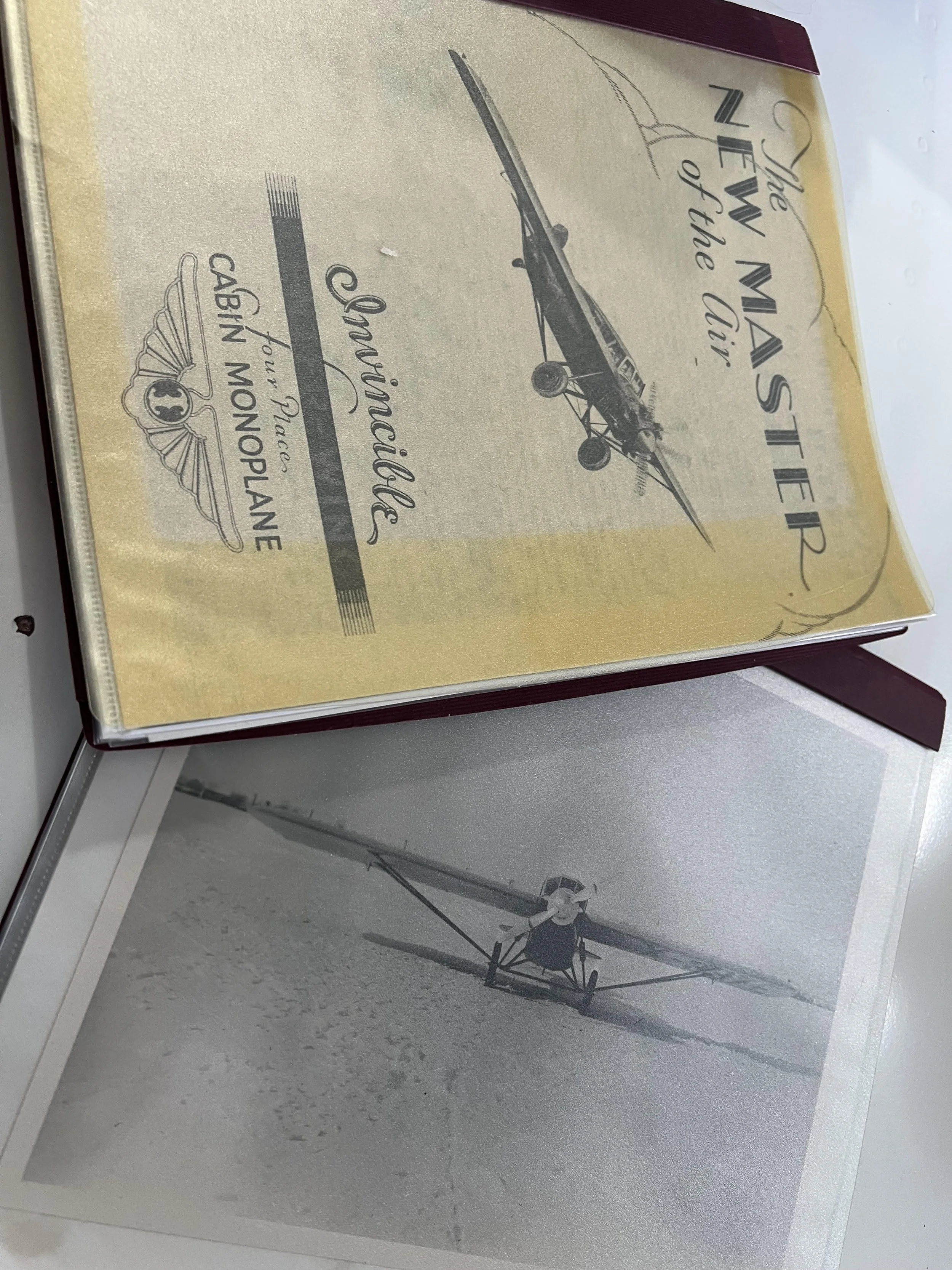 A vintage magazine titled 'The Master of the Air', featuring a black and white photo of a vintage airplane. There is also a black and white photograph of a person in a glider on the surface below the magazine.