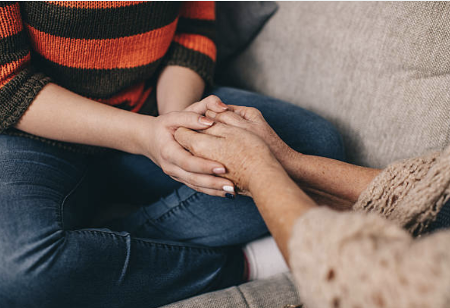 Two women holding hands, one appears older with tanned skin and the other younger, in a moment of comfort and support.