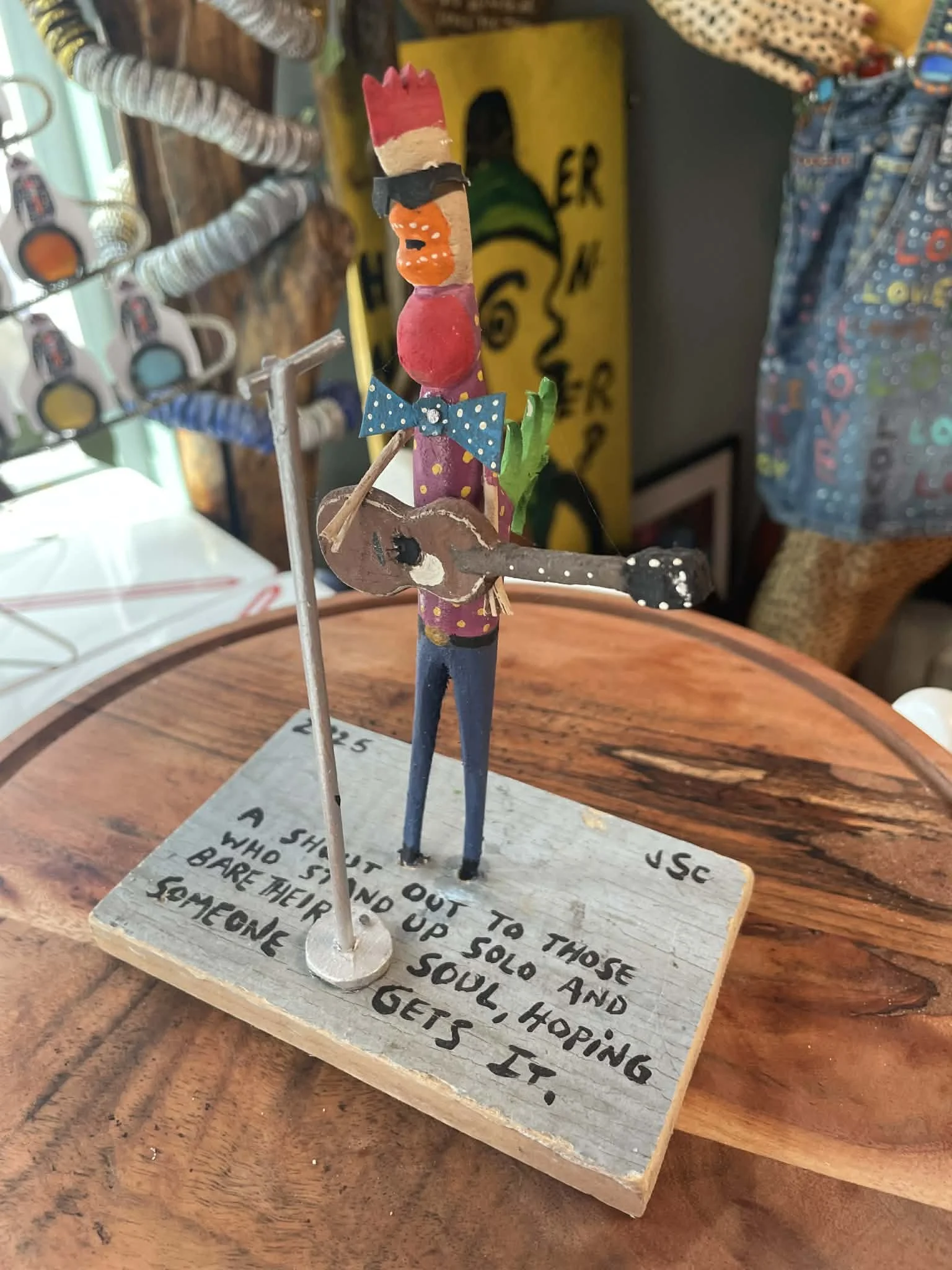 A whimsical handcrafted figurine of a person playing a guitar on a wooden base with handwritten poem.