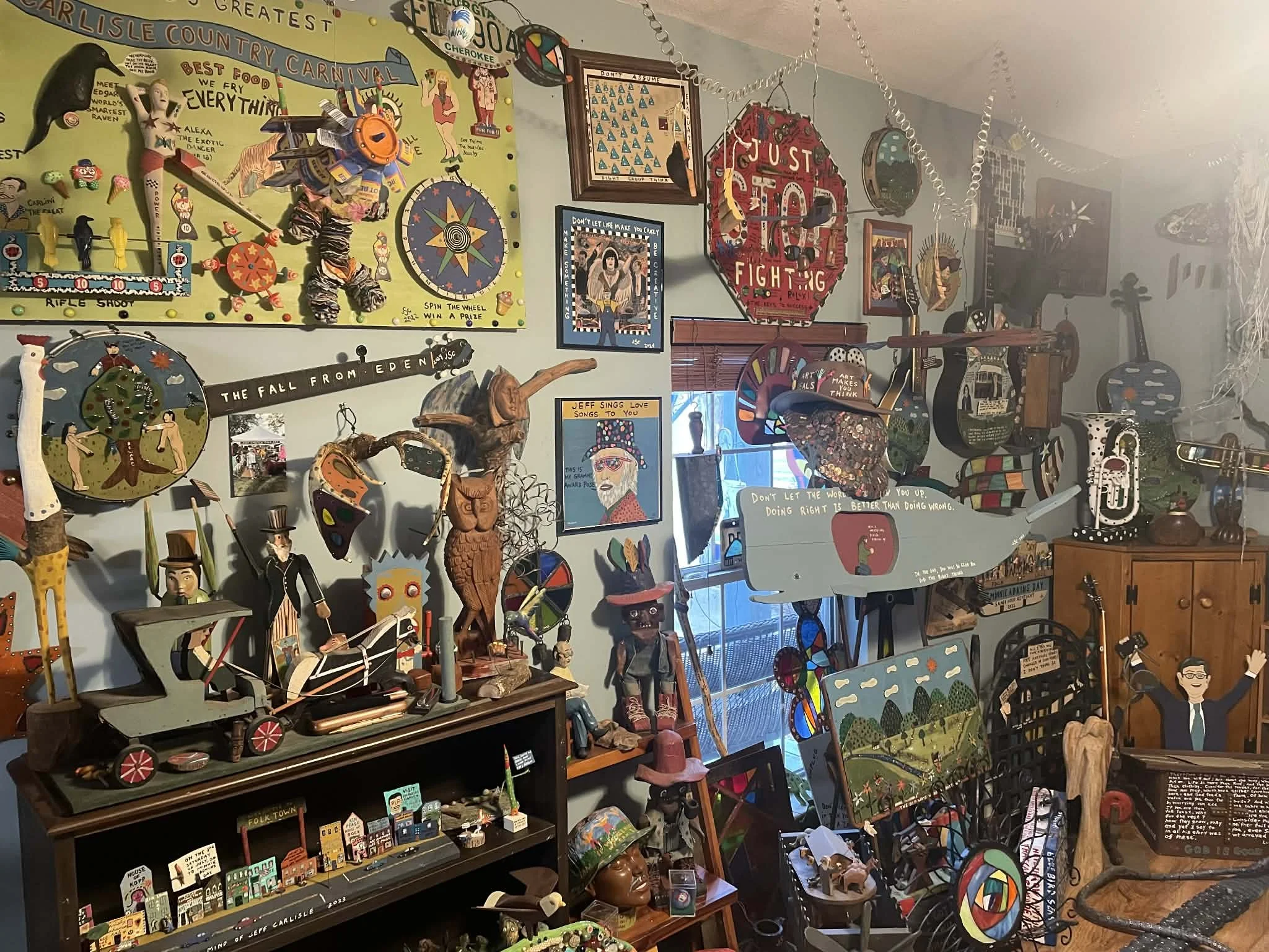 A wall decorated with various colorful artwork, signs, and eclectic decorations, including guitars, framed pictures, painted signs with motivational messages, and whimsical sculptures in a vibrant, artistic space.