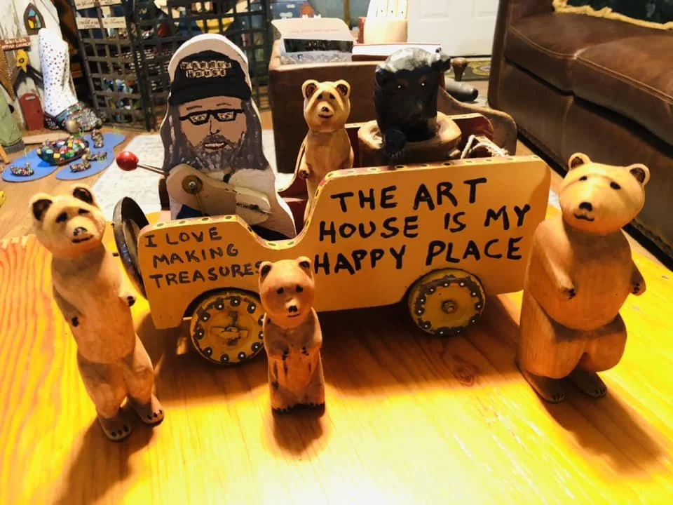 Wooden animal figurines, including bears and a pig, surround a decorative cart with a sign that reads, "The art house is my happy place" and a smaller sign that says, "I love making treasures." The scene is on a wooden table with various craft items 