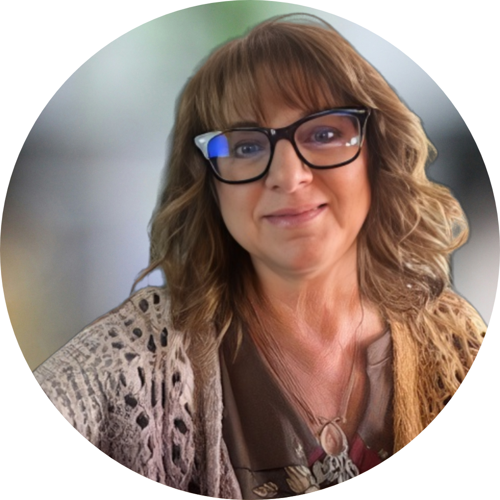 A woman with wavy brown hair, wearing glasses with a blue nose pad, smiling slightly, dressed in a leopard print shawl and a brown top with a necklace, against a blurred green background.