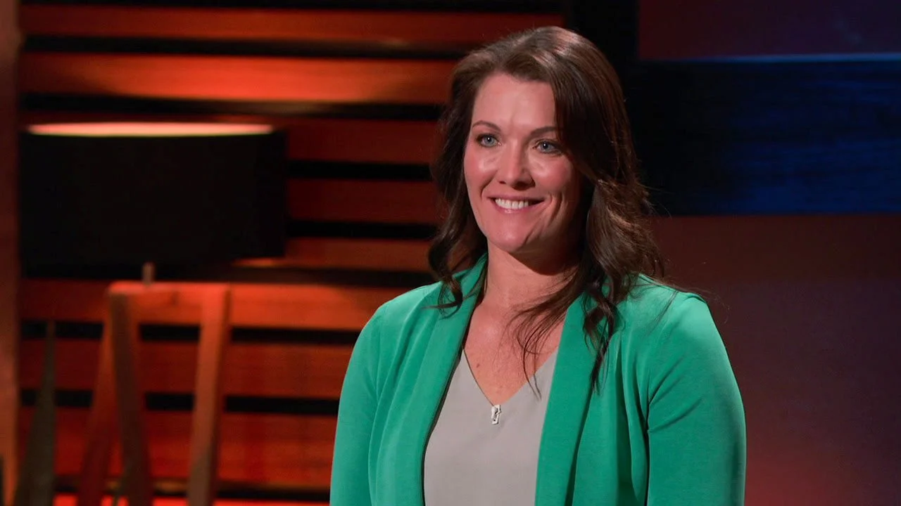 Beth Benike on the set of Shark Tank, wearing a teal blazer over a light top..