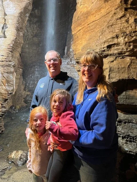 Family of four smiling in front of a waterfall inside a cave or cavern.