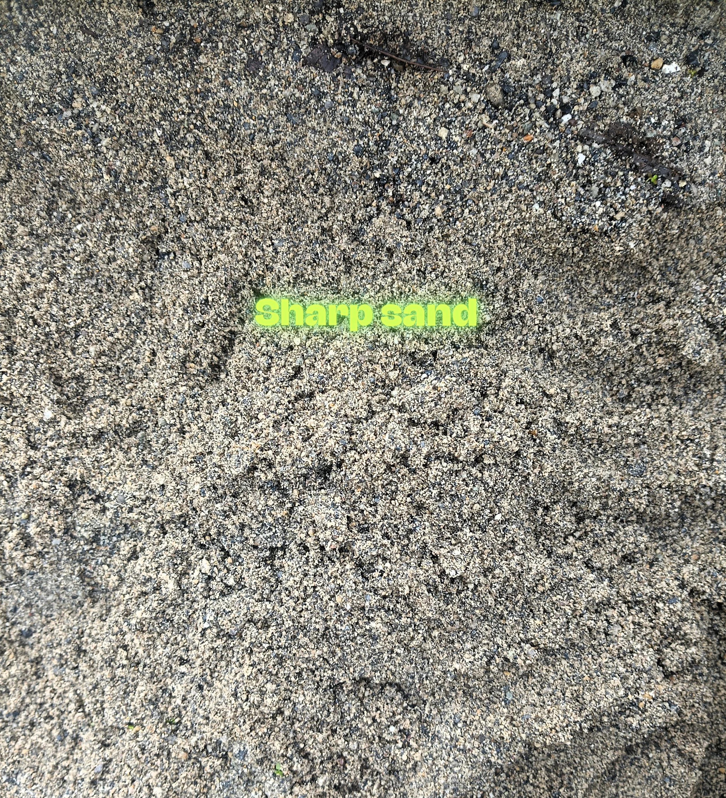Close-up of sandy beach with coarse, sharp sand texture and a faint text overlay that says 'Sharp sand' in bright yellow-green color.