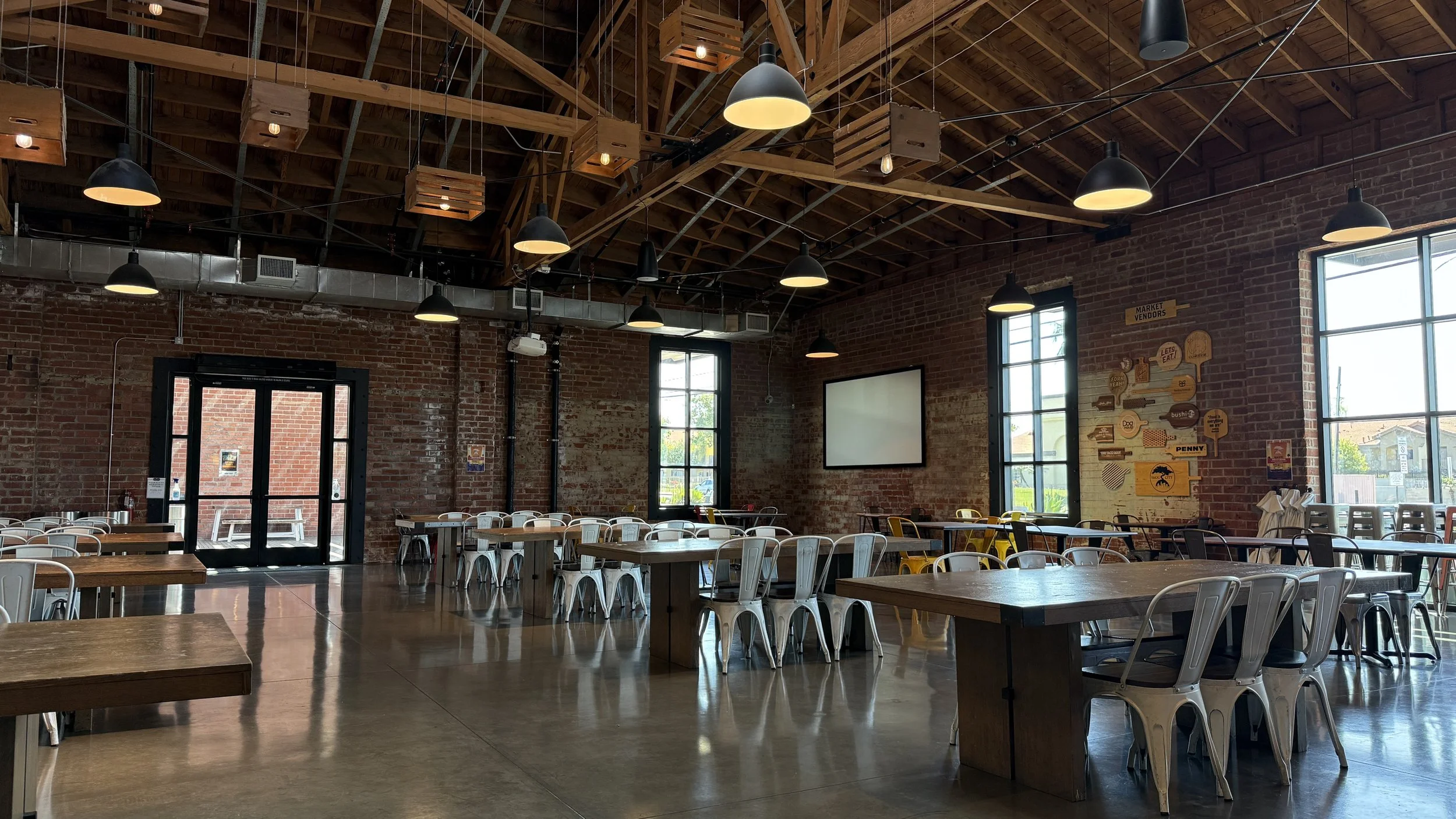 Communal table seating area on a taproom floor with six metal chairs at each.