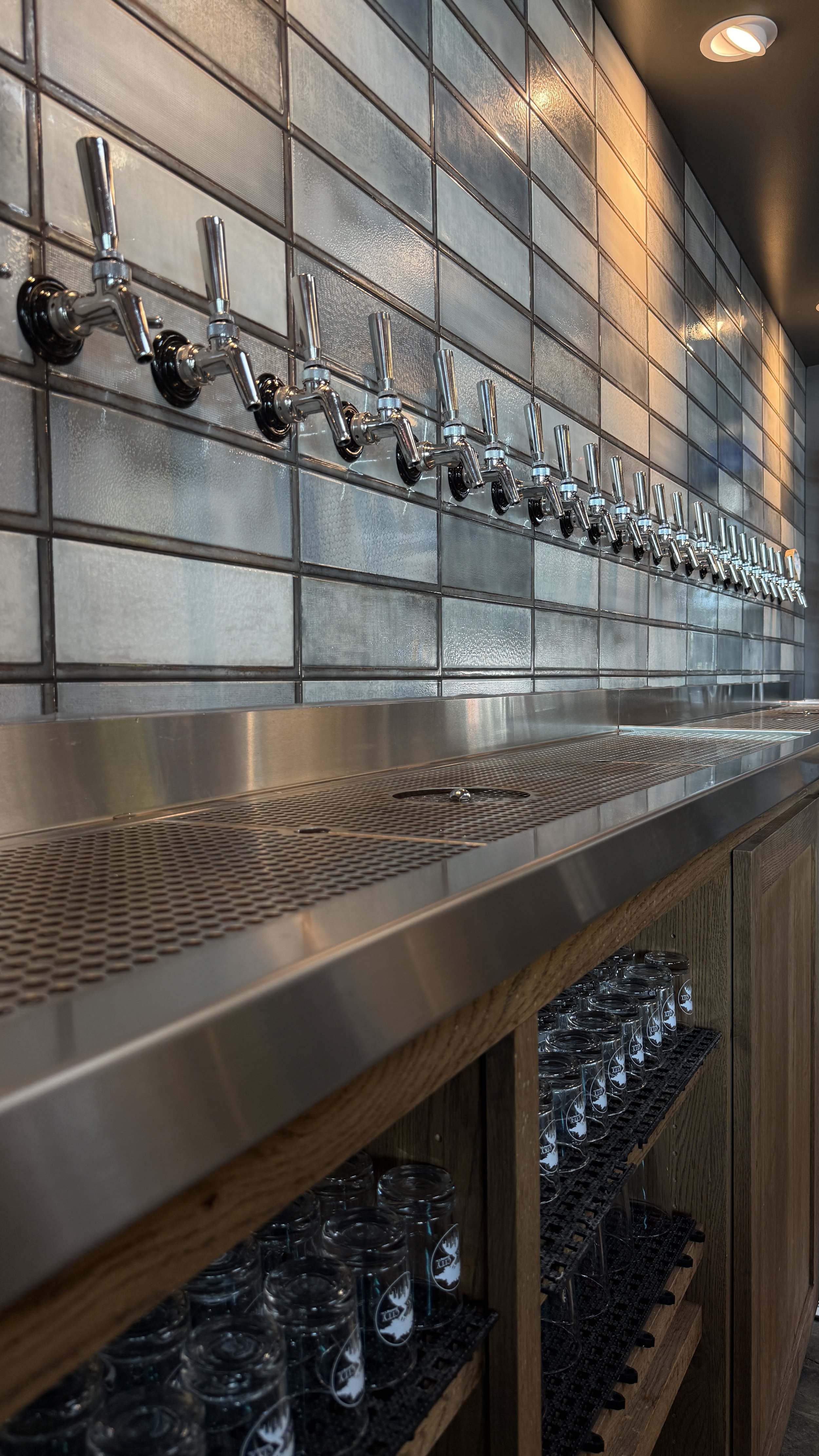 Metal beer taps along a tiled wall.