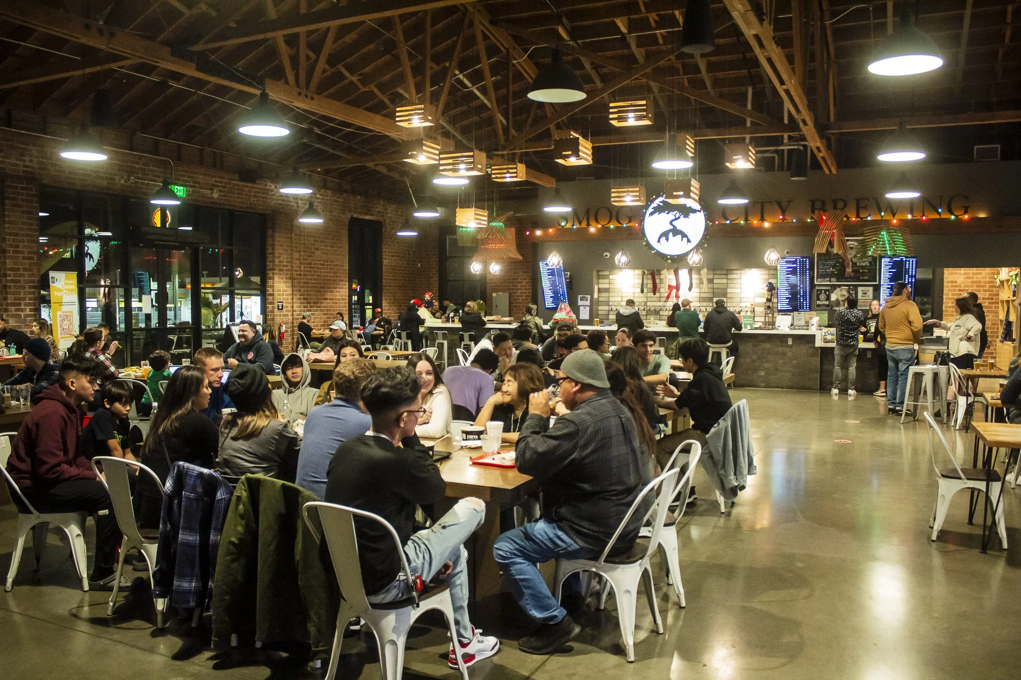 Large crowd of patrons sitting at tables on the taproom floor with Christmas lights above in the background.