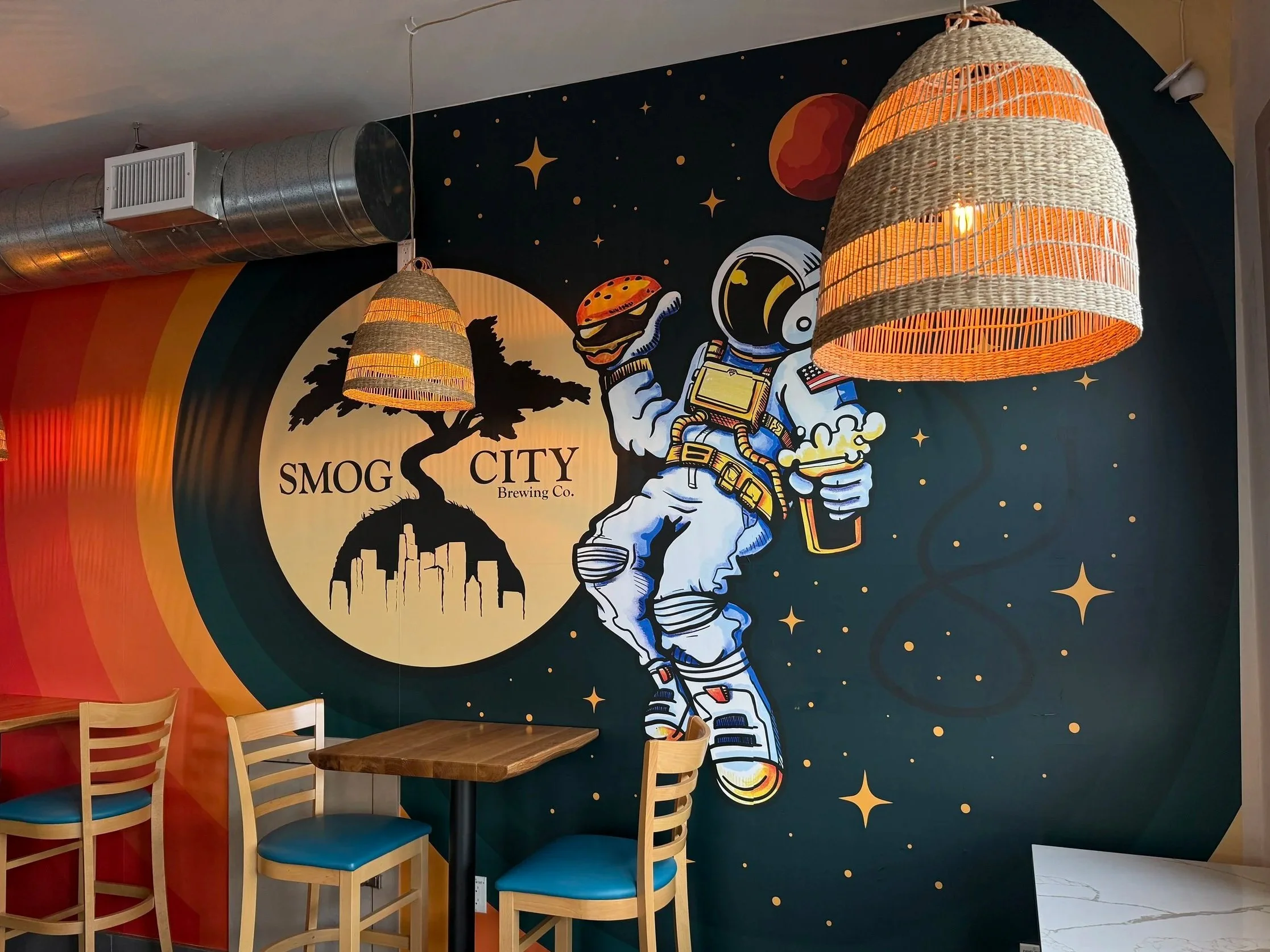 Interior wallpaper of Smog City Heights featuring an astronaut holding a burger and a beer floating in front of the Smog City logo.