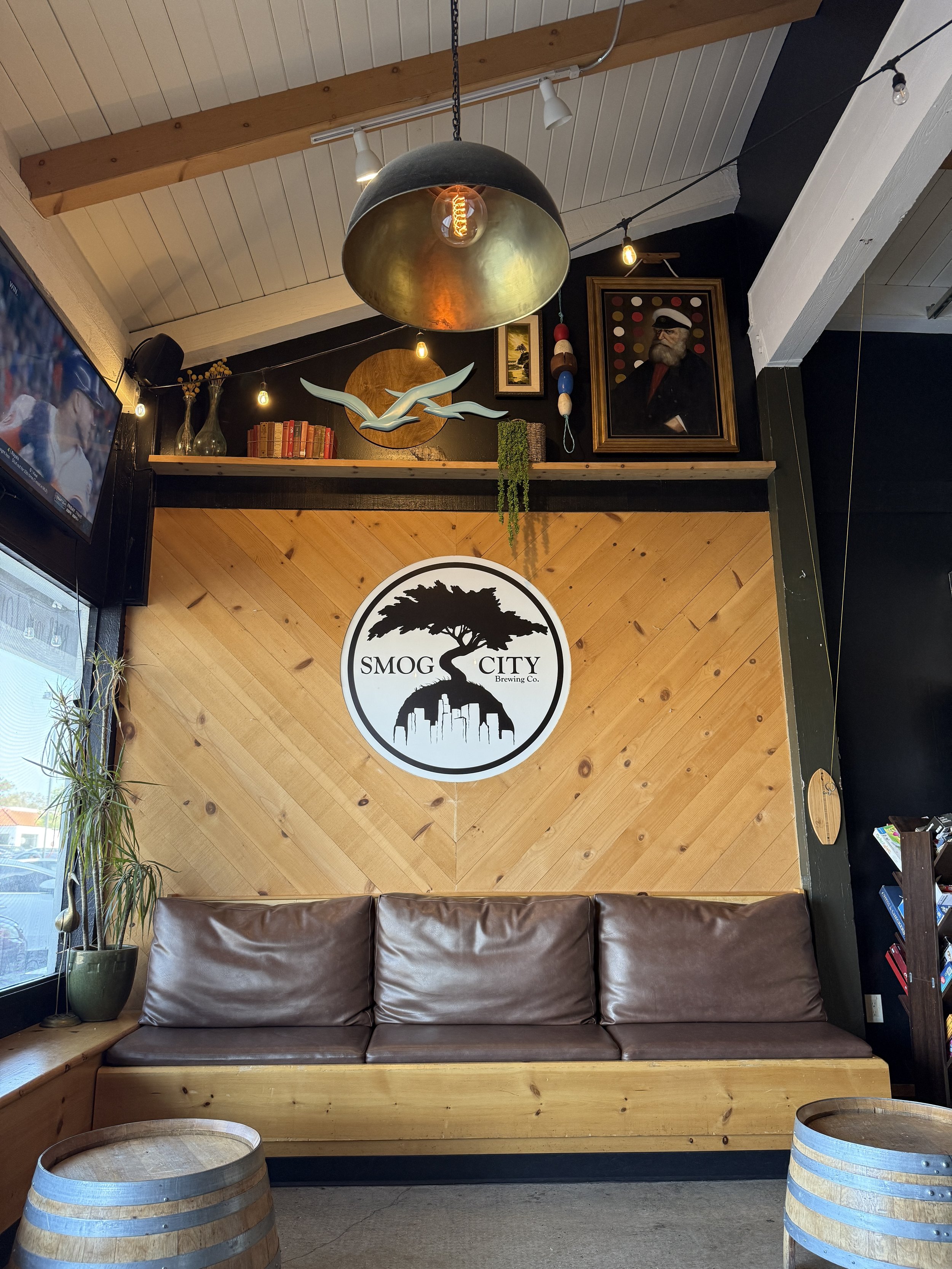 Leather upholstered couch in the lounge area of Smog City West taproom with the Smog City logo sign above it on the wall.