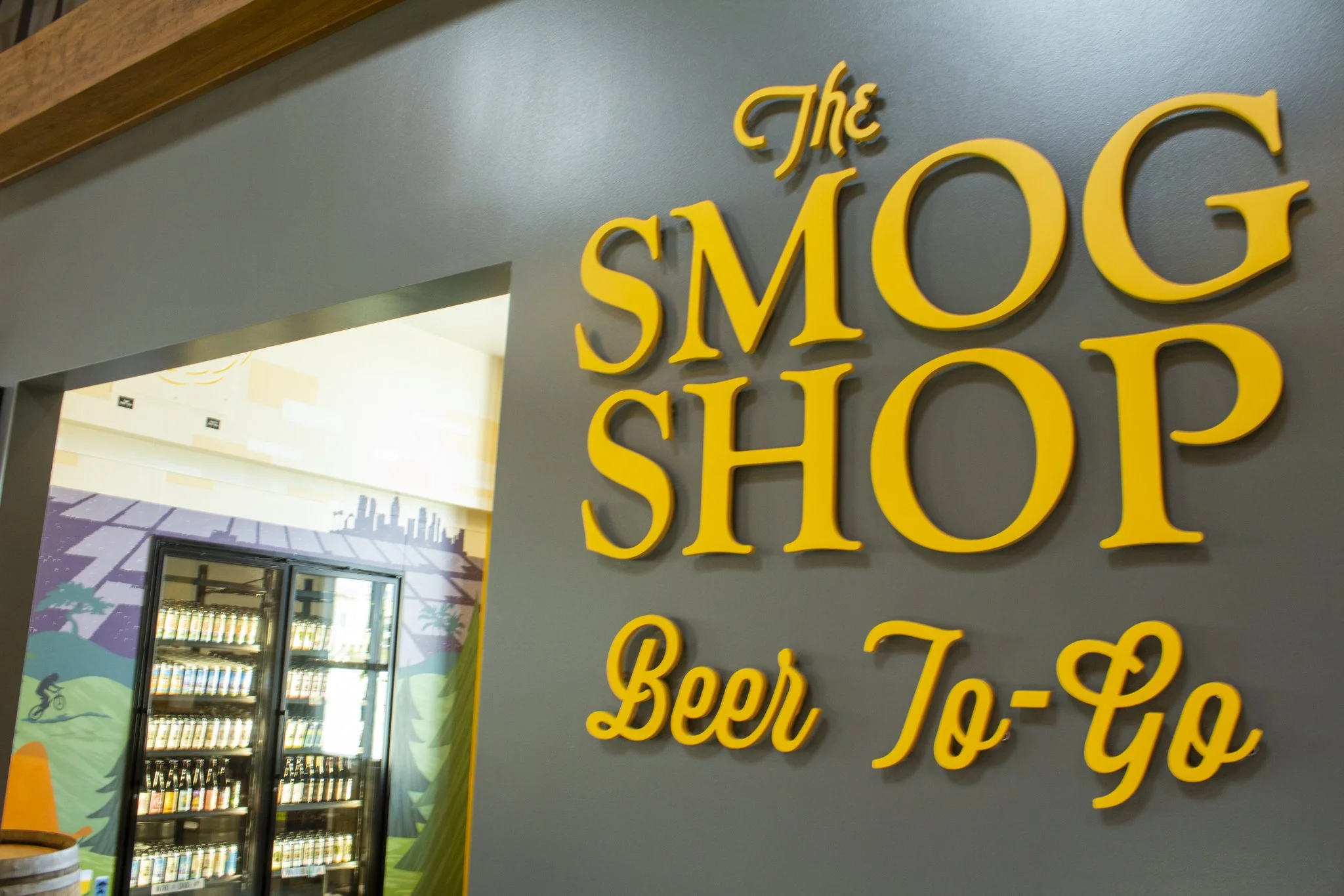 "The Smog Shop: Beer To-Go" sign in yellow on a green wall.