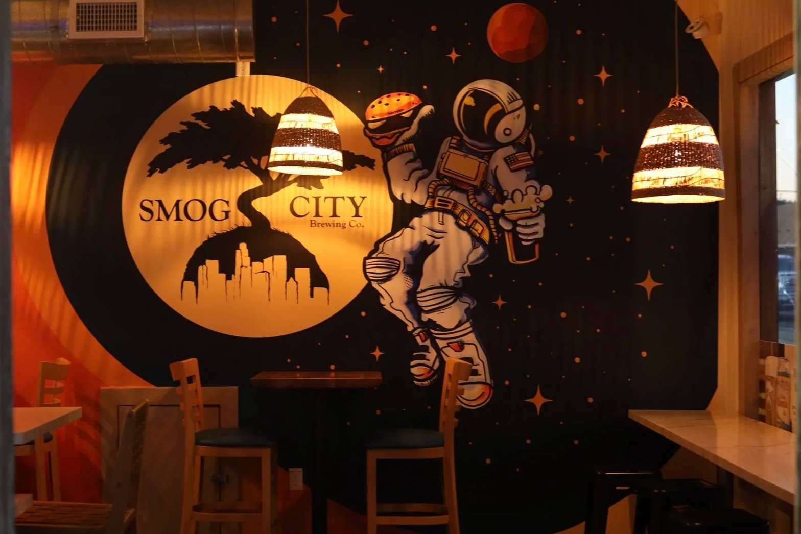 Interior wallpaper of Smog City Heights featuring an astronaut holding a burger and a beer floating in front of the Smog City logo.