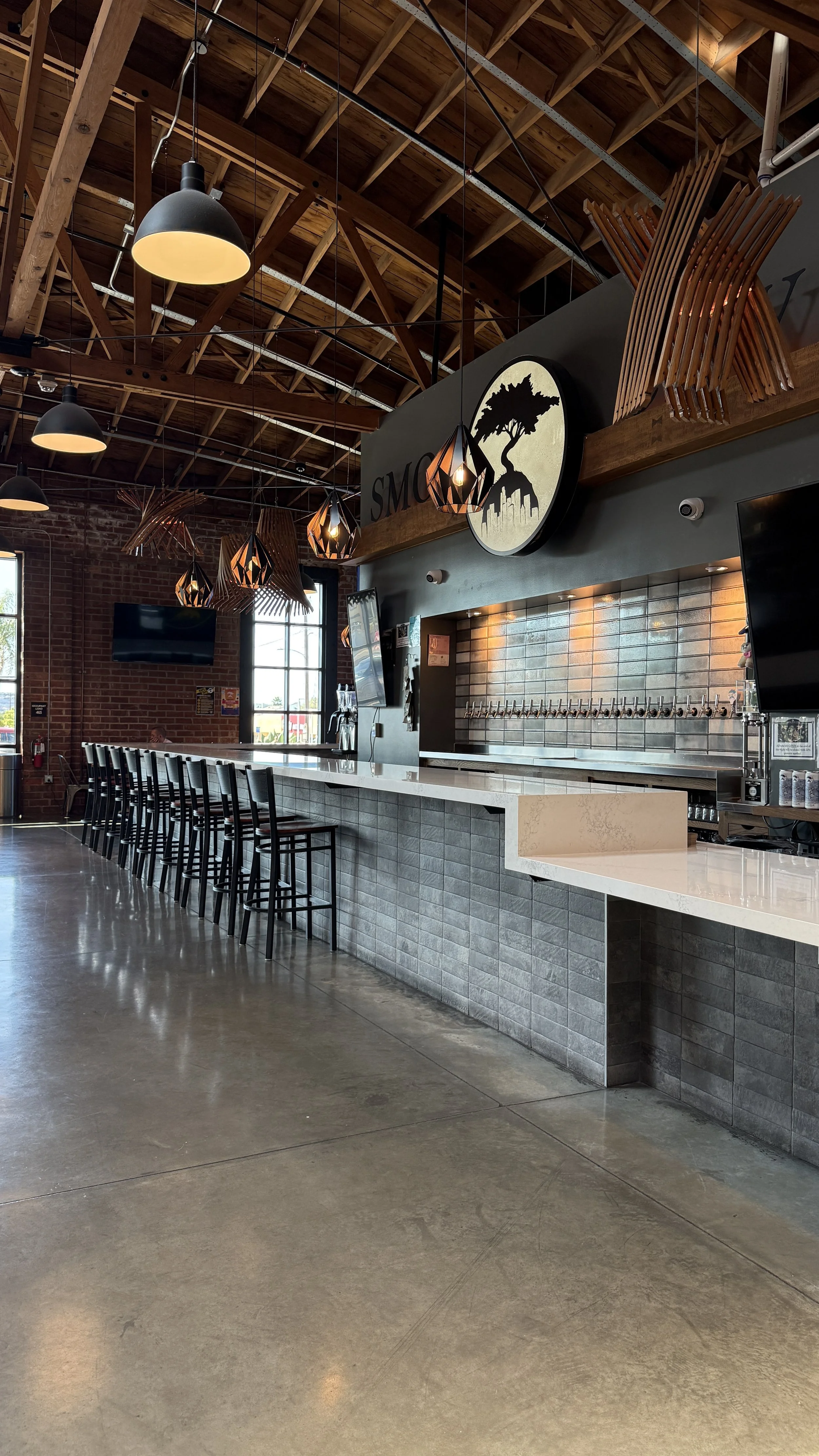View of one side of the bar at Smog City Glendora with stools, brick wall in background, and lights hanging overhead.