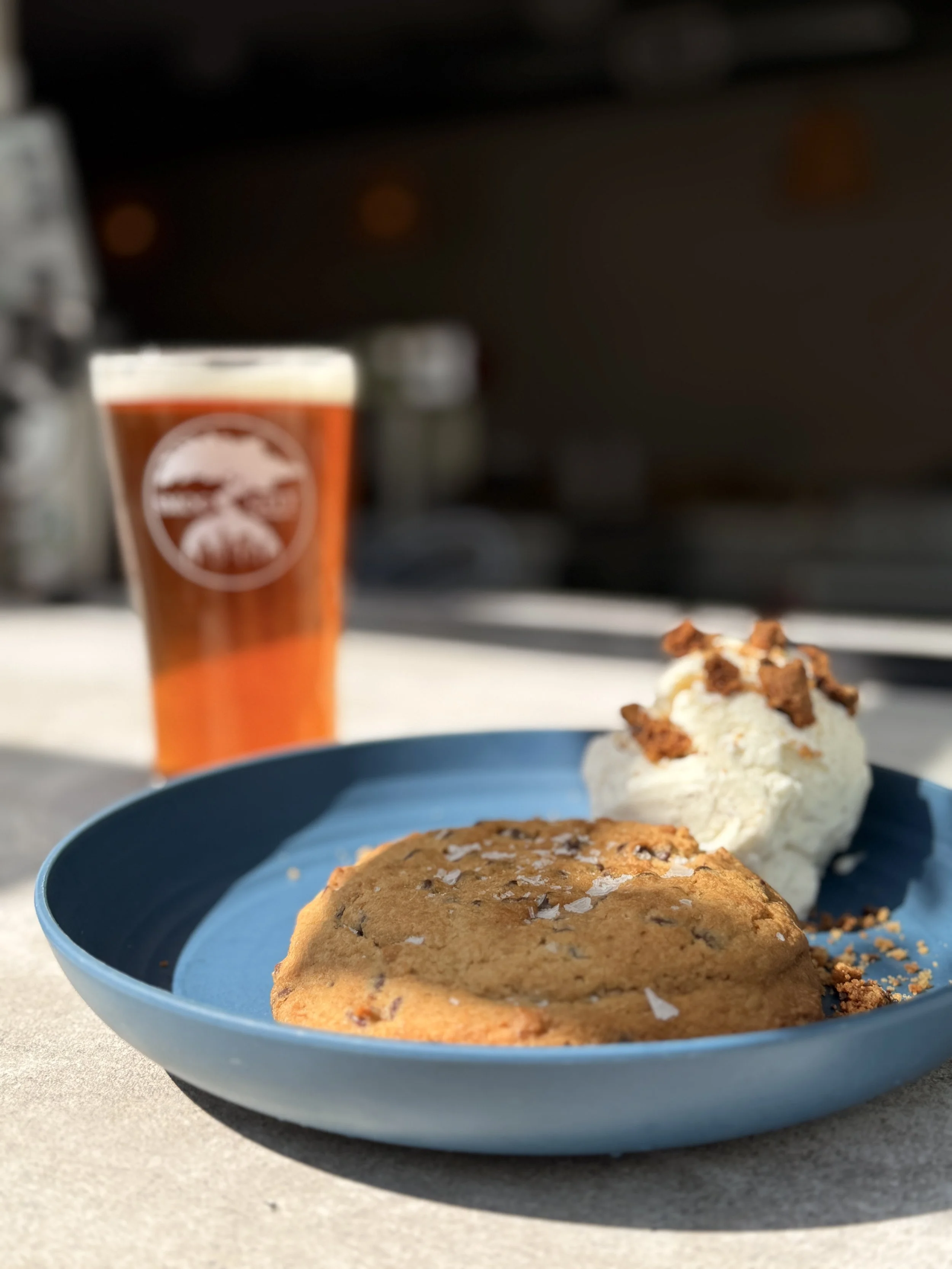 Close up of a cookie on a blue plate with a pint of beer in the background.