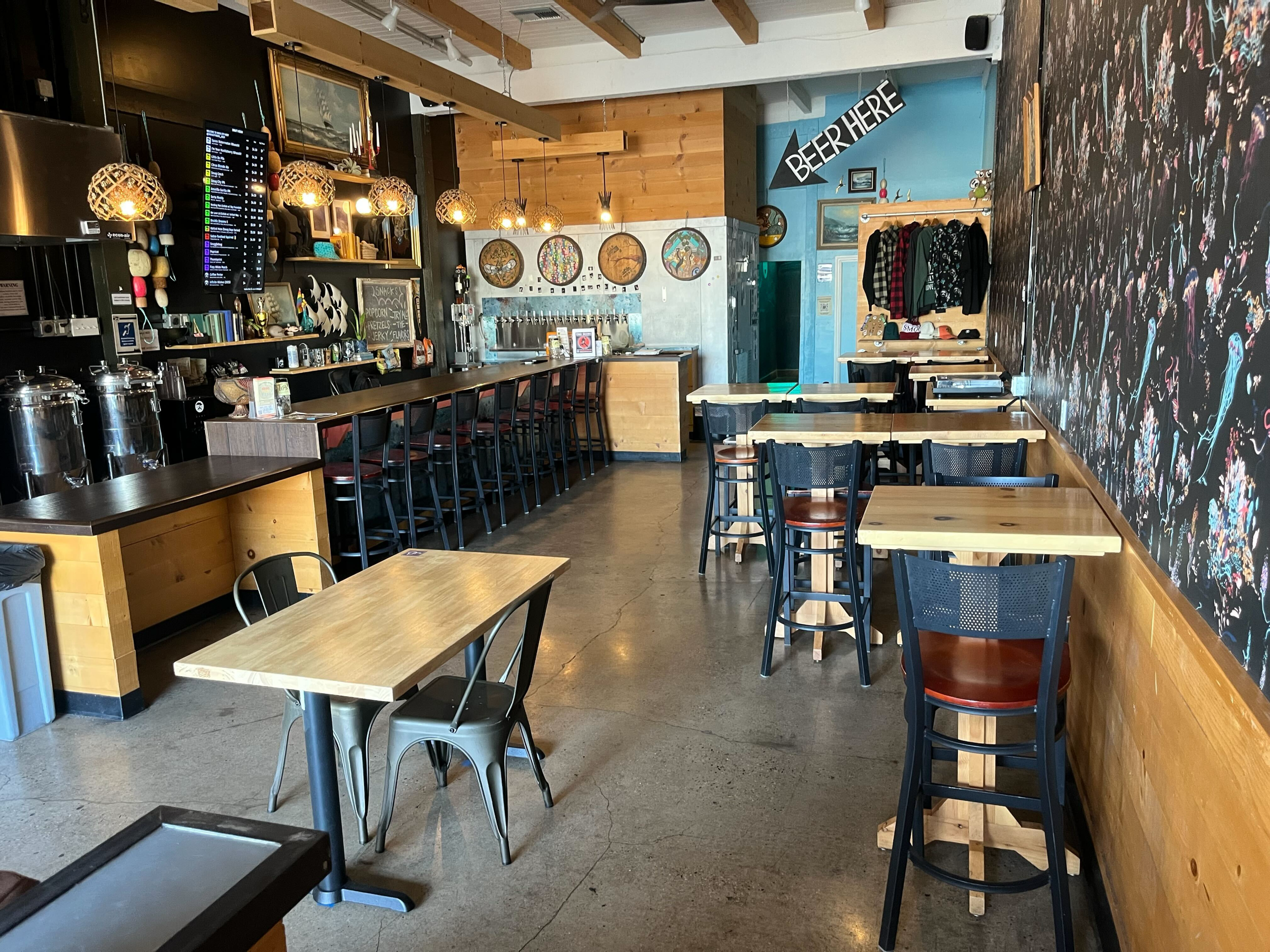 Empty cafe with wooden furniture, high bar seats, and a textured chalkboard wall with colorful paint splatters.