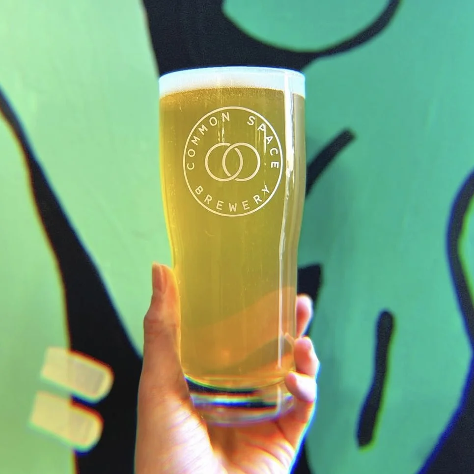 Hand holding a filled Common Space Brewery beer glass.