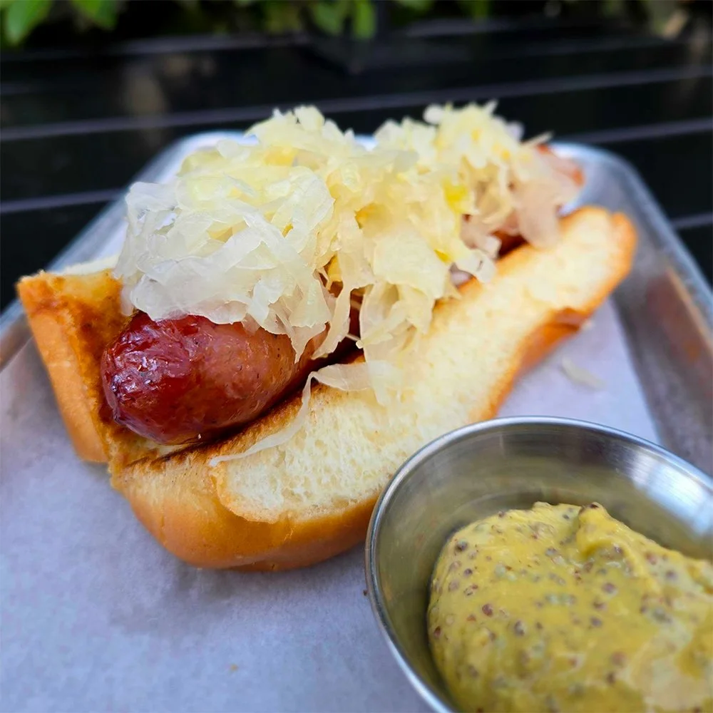 Bratwurst on a bun with sauerkraut and a container of brown mustard.