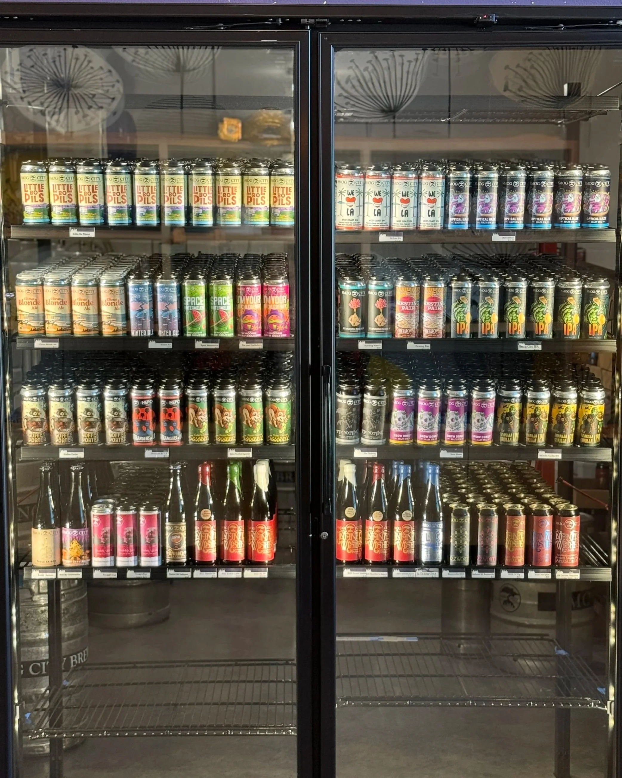 Refrigerator with four shelves stocked with various bottles and cans of beer.