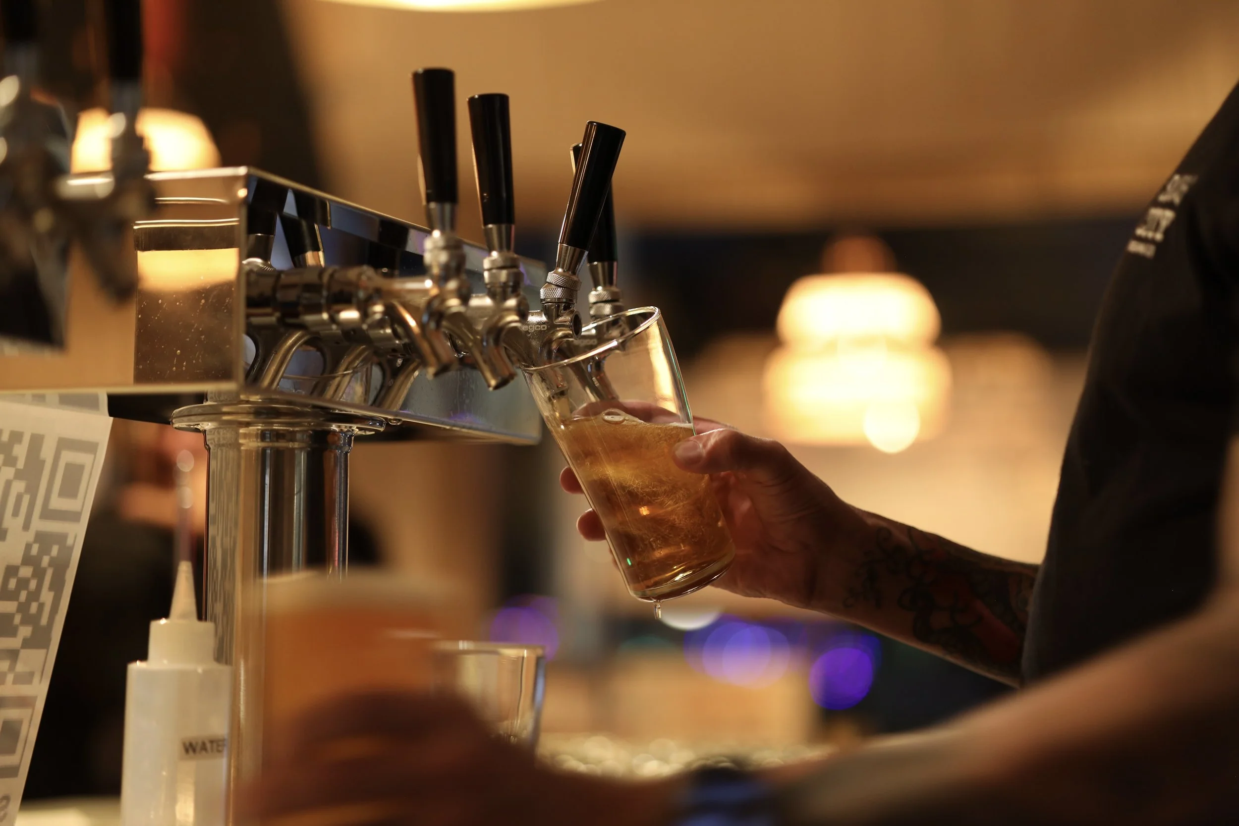 Hand holding a pint glass that is being filled with beer from a tap handle.