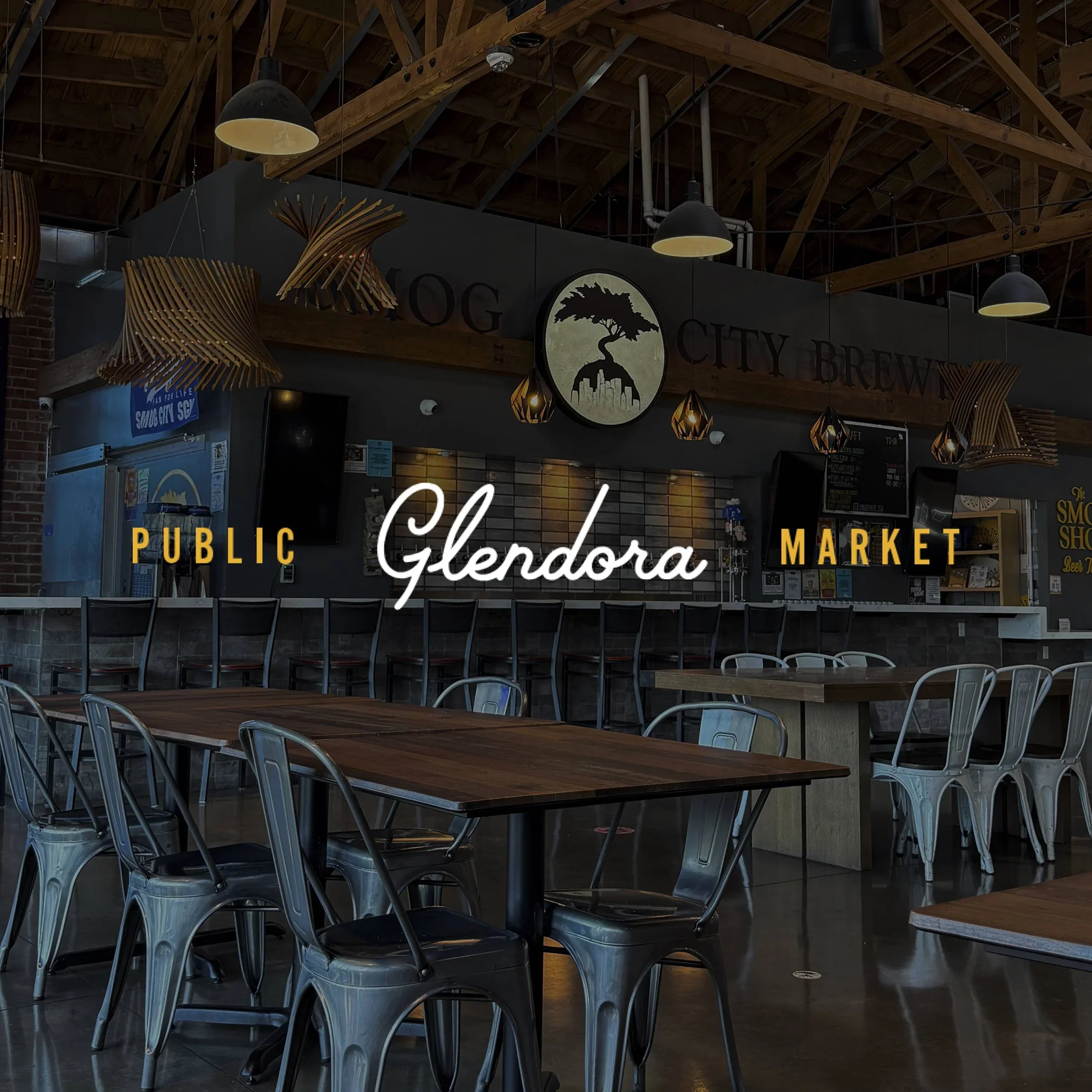 Interior of Glendora Public Market featuring wooden tables, metal chairs, bar seating, and industrial-style lighting fixtures in a brewery or market setting.