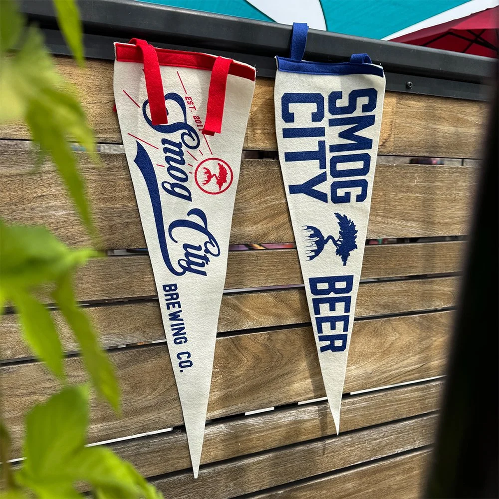 Two Smog City Brewing pennants hanging from an outdoor wall.